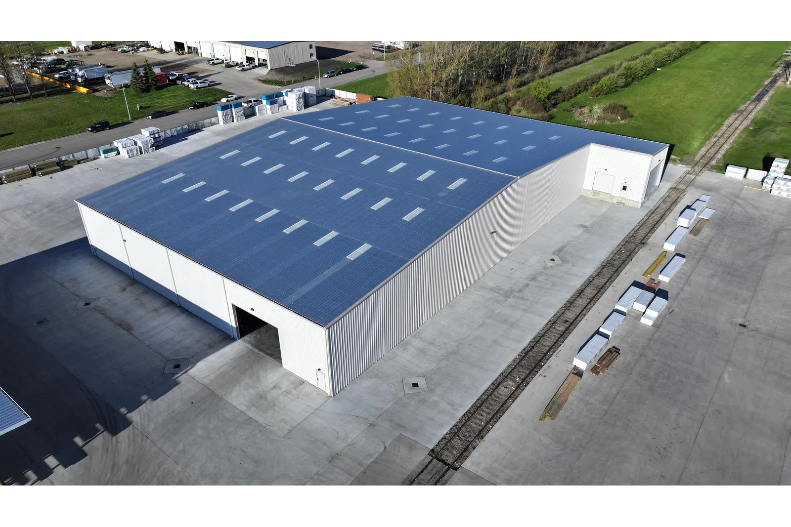A large industrial warehouse with a blue roof and surrounding concrete yard in an open area.