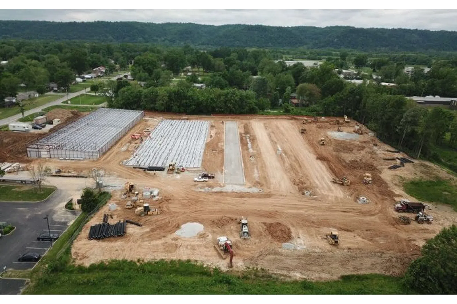 Aerial view of a construction site with machinery, foundation work, and surrounding greenery.
