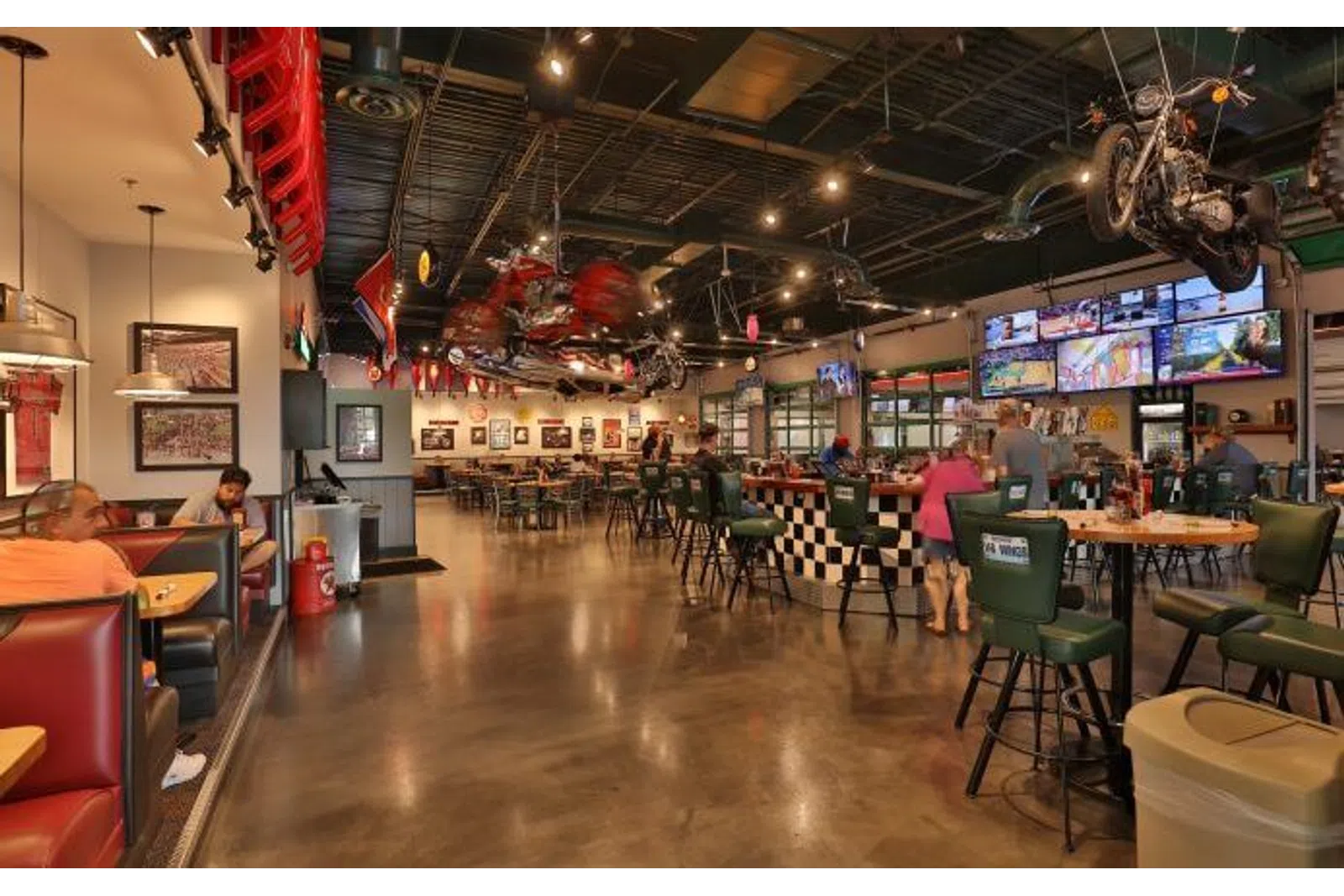 Spacious motorcycle-themed bar and restaurant with patrons, multiple TVs, and unique decor including hanging motorcycles.