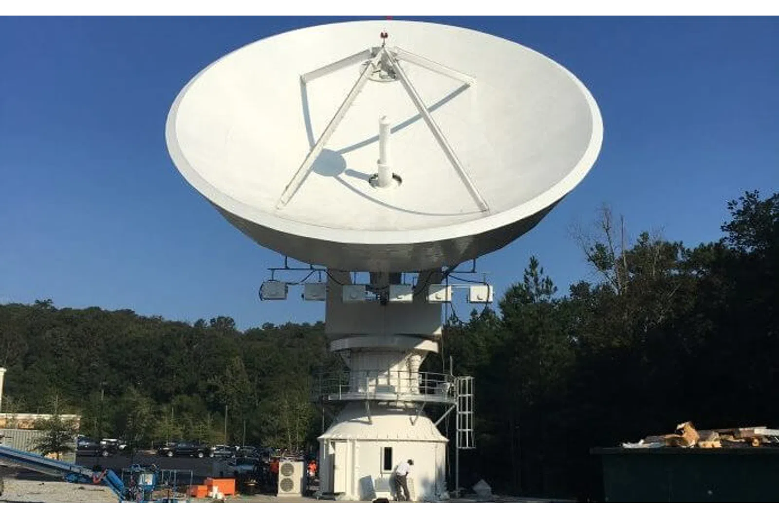 Large white satellite dish antenna mounted outdoors with trees and clear sky in background