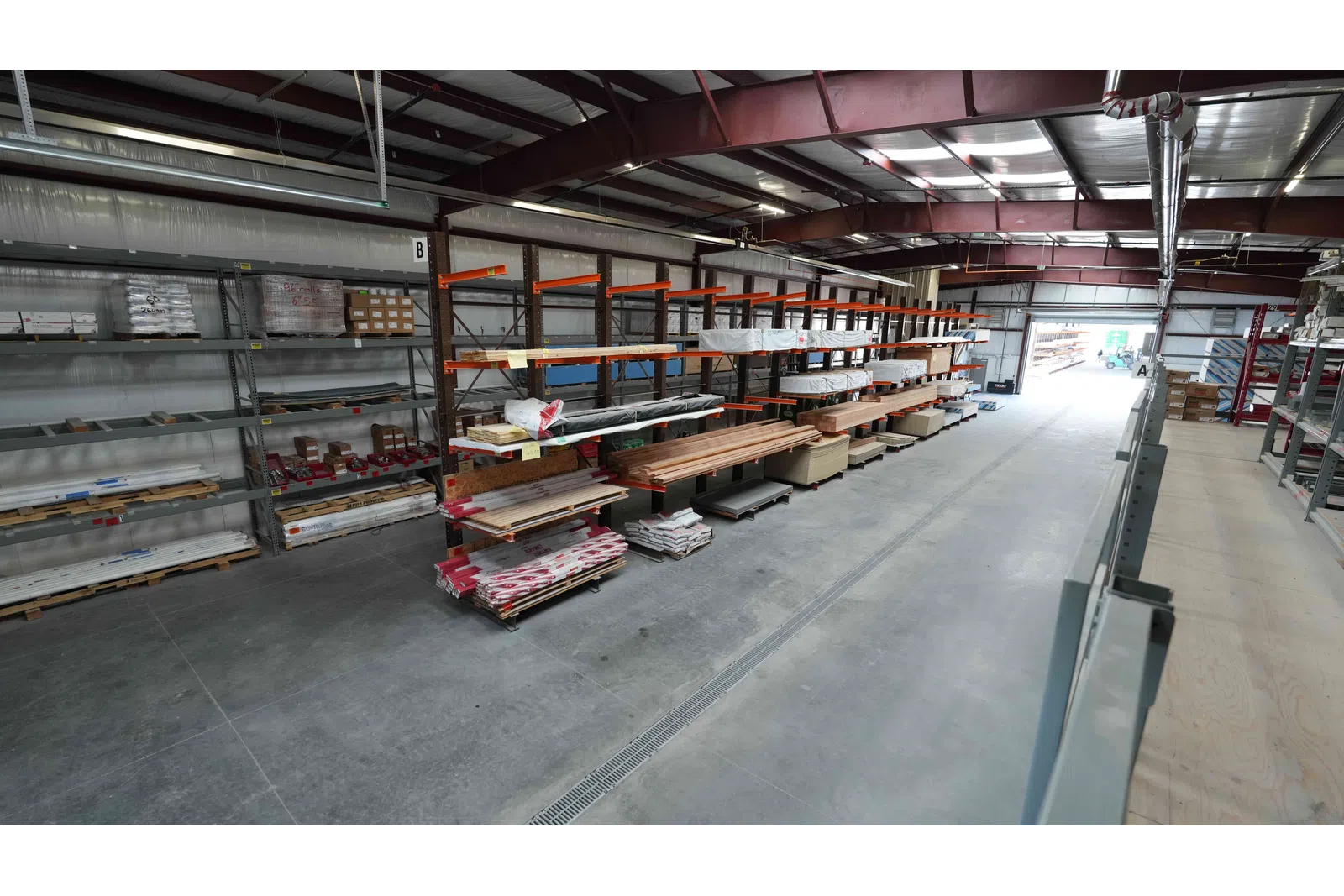 Warehouse interior with metal racks holding wood planks and building materials in an organized industrial space.
