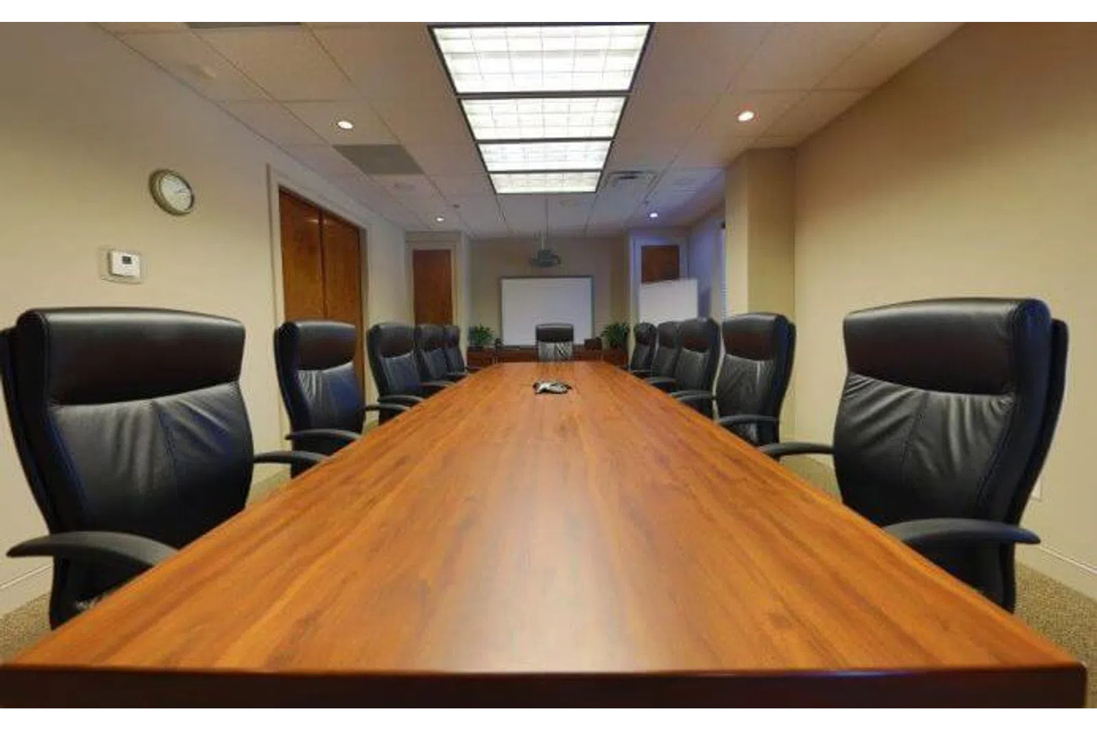 Empty modern conference room with a long wooden table and black leather executive chairs under ceiling lights.