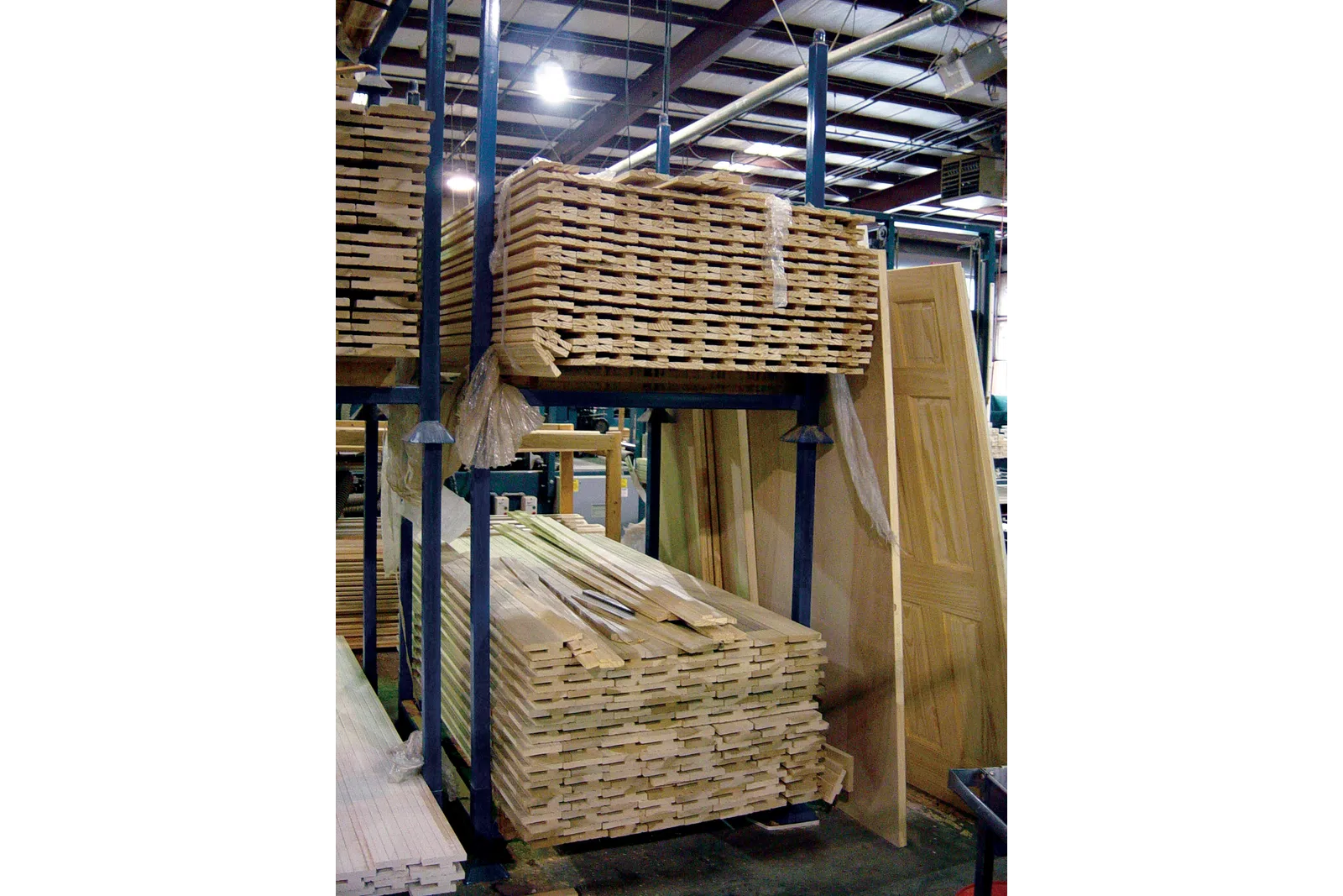 Stacks of wooden planks and doors stored on metal racks inside a woodworking factory warehouse.