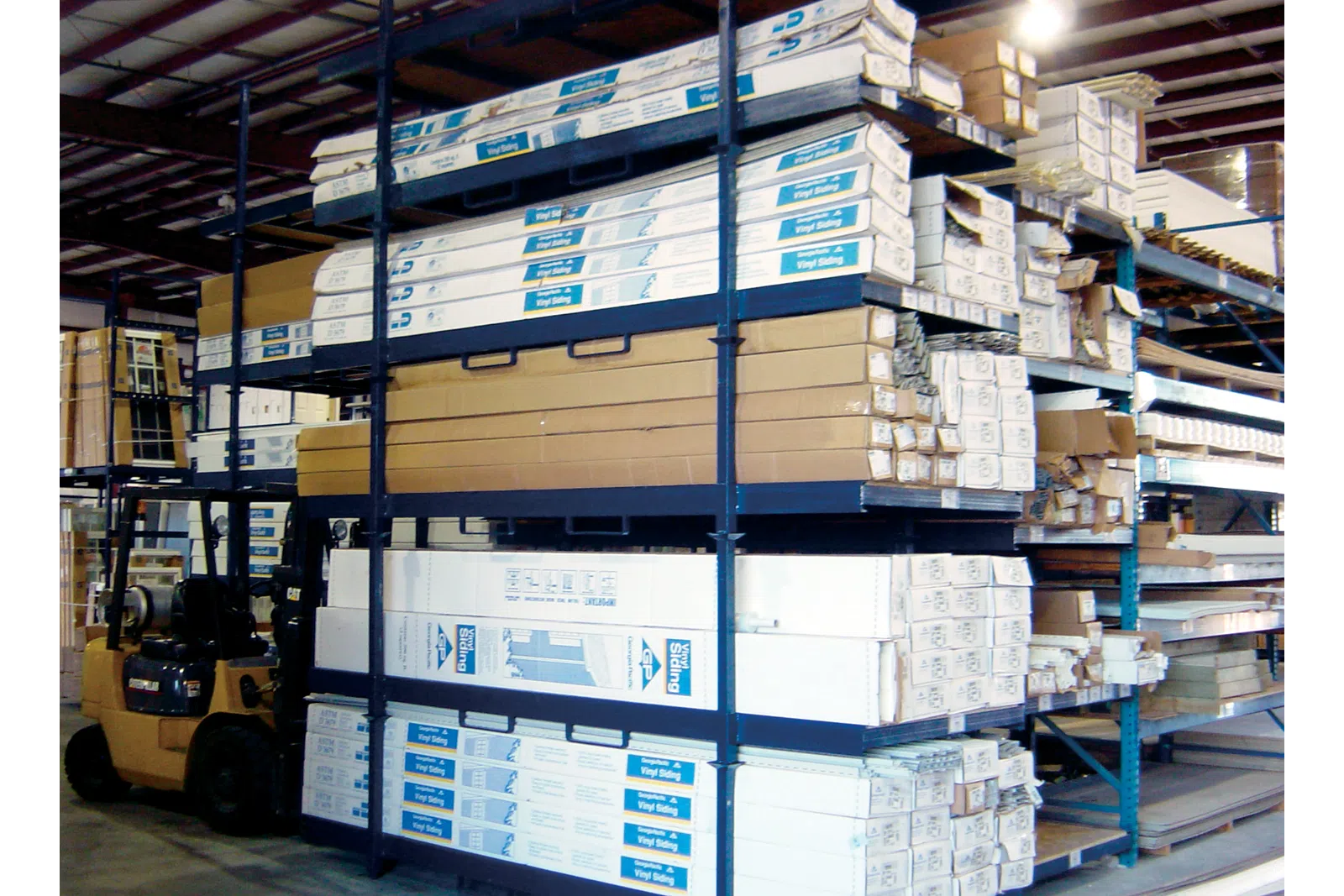 Warehouse shelving stocked with boxed vinyl siding and construction materials with forklift nearby
