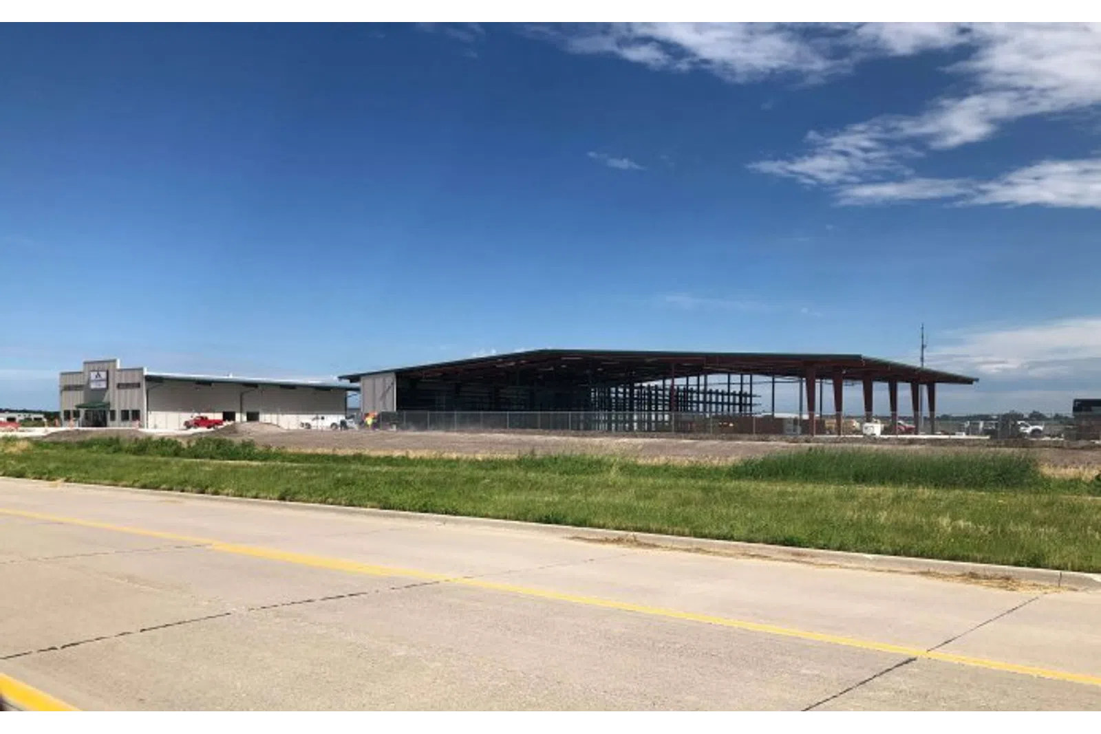 Construction site with steel frame building and adjacent warehouse under blue sky and scattered clouds