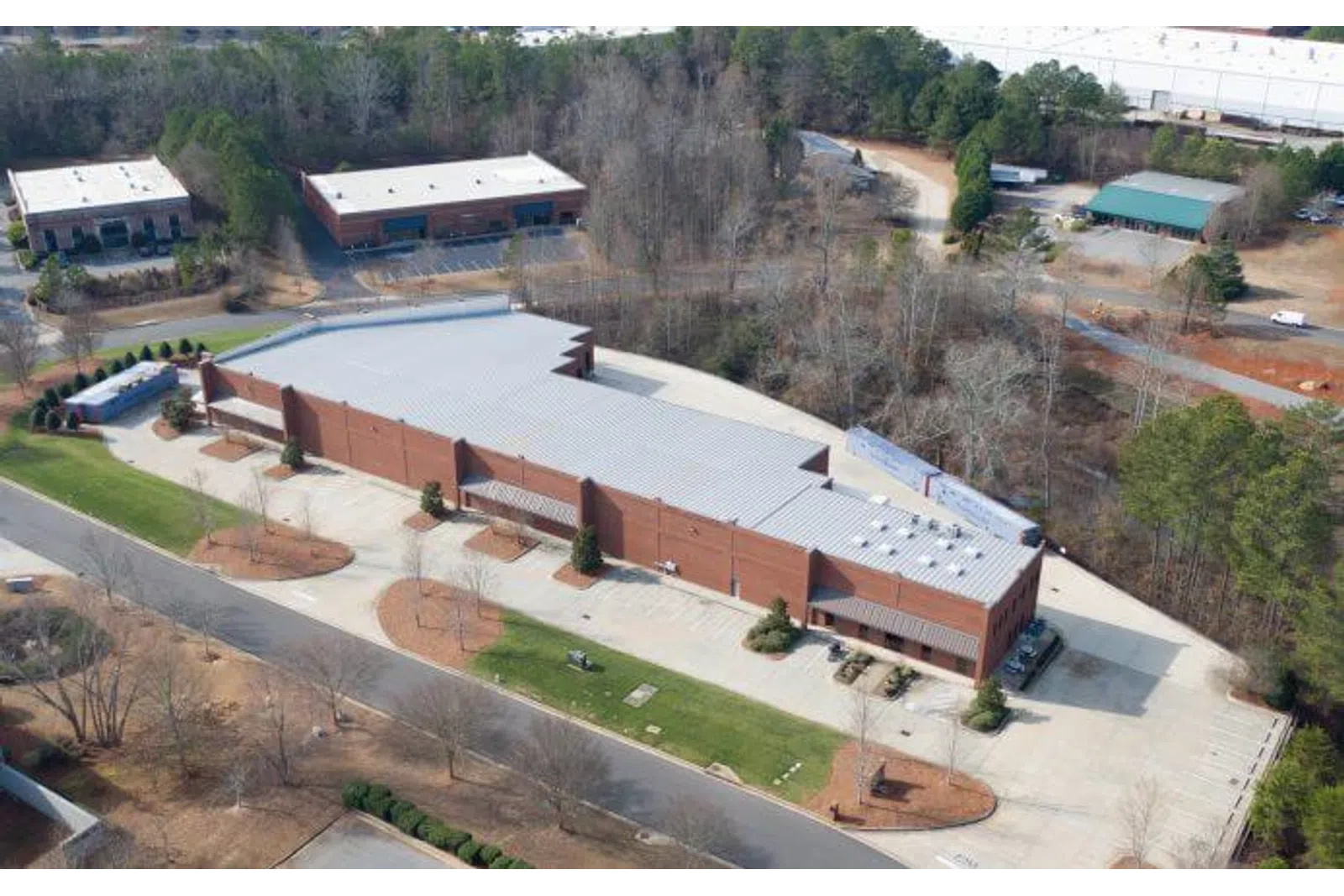 Aerial view of a large brick commercial building surrounded by parking areas and trees in a suburban setting.