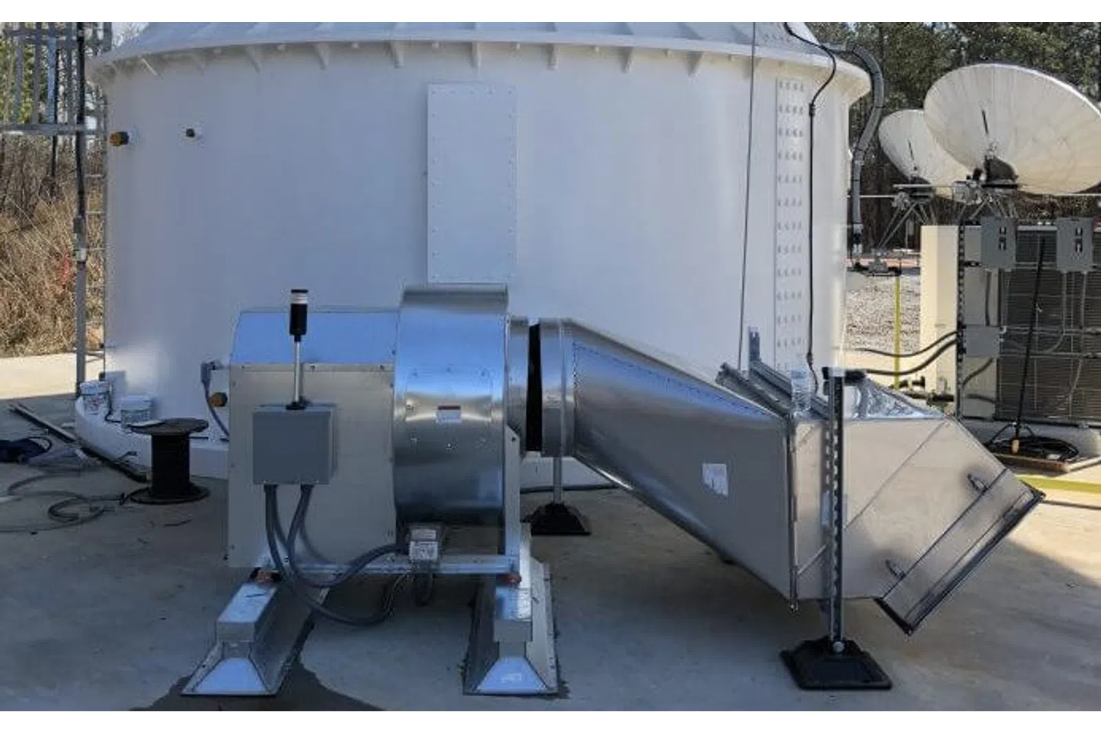 Industrial ventilation system with metal ducts and fan installed on concrete surface outside a building.