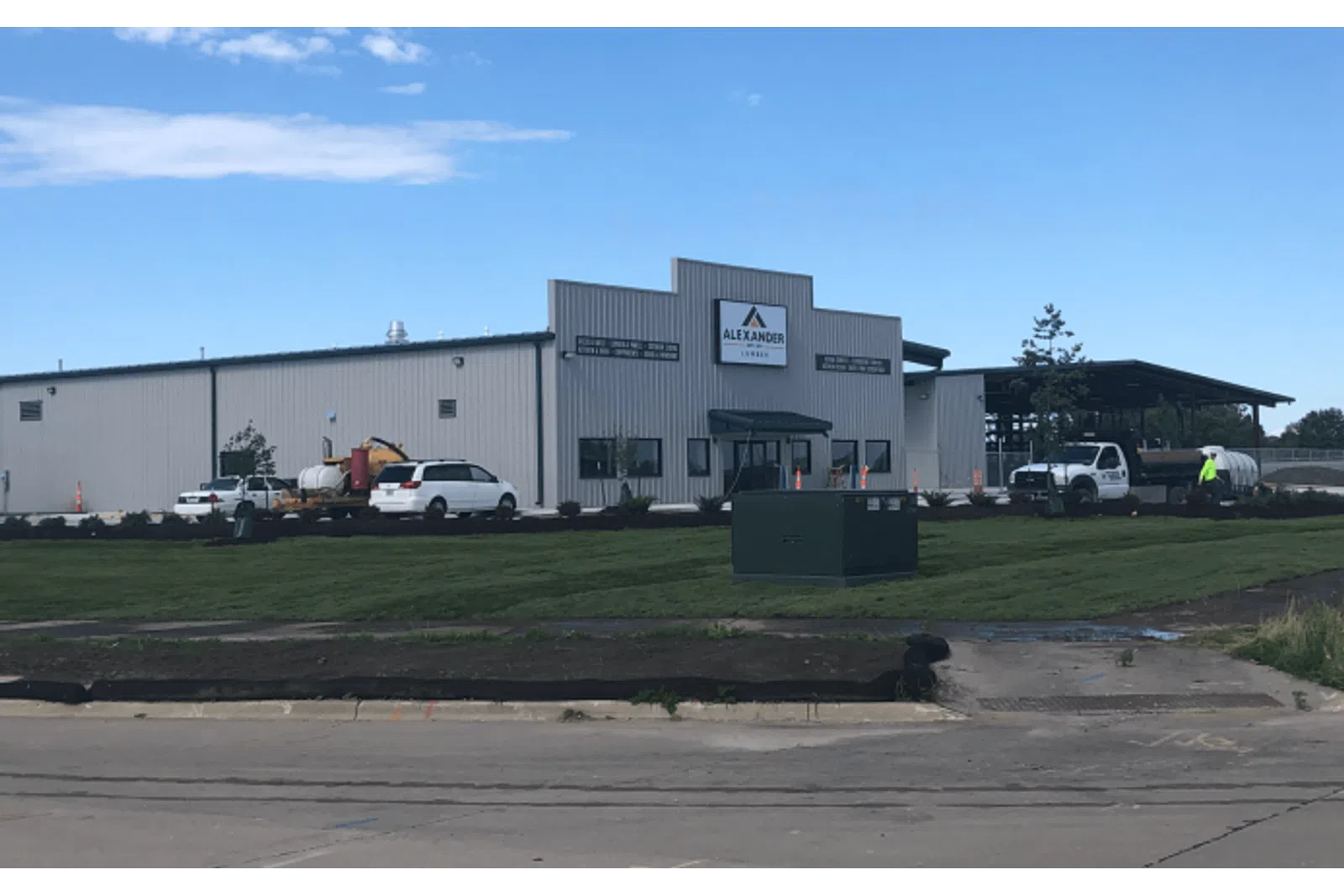 Industrial warehouse building with Alexander Leasing signage, vehicles, and a freshly landscaped lawn under a clear blue sky.