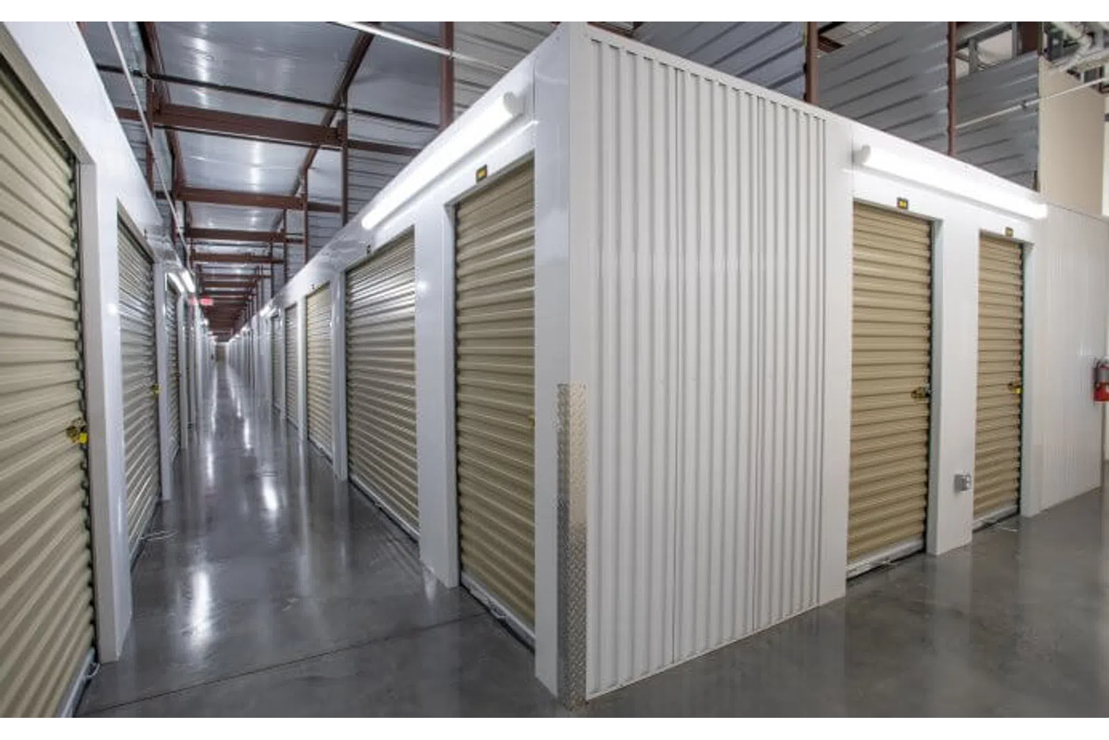 Indoor storage facility with metal roll-up doors along clean polished concrete floors and metal roof framework.