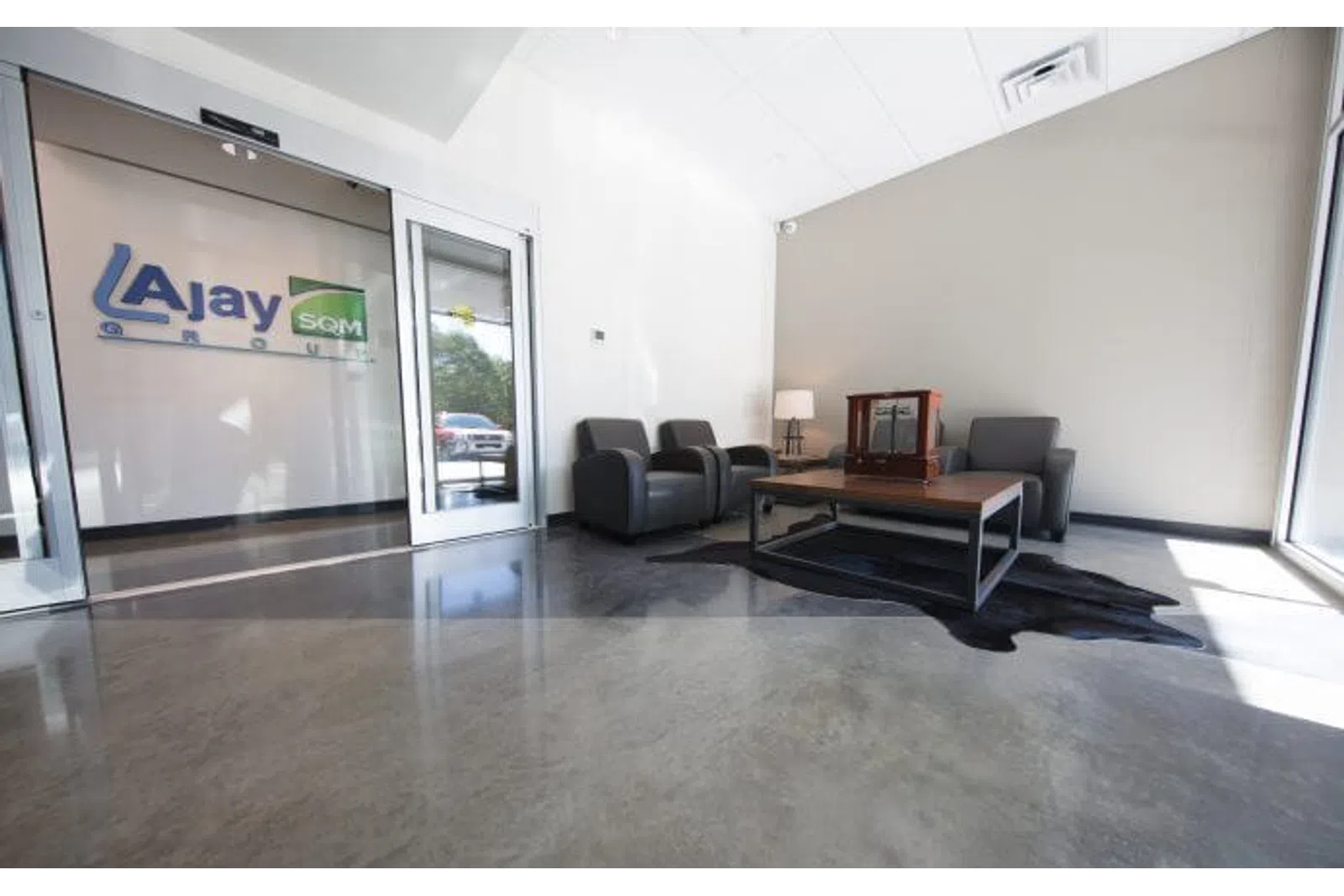Modern office lobby with leather chairs, wooden coffee table, and Ajay Group logo on glass wall.