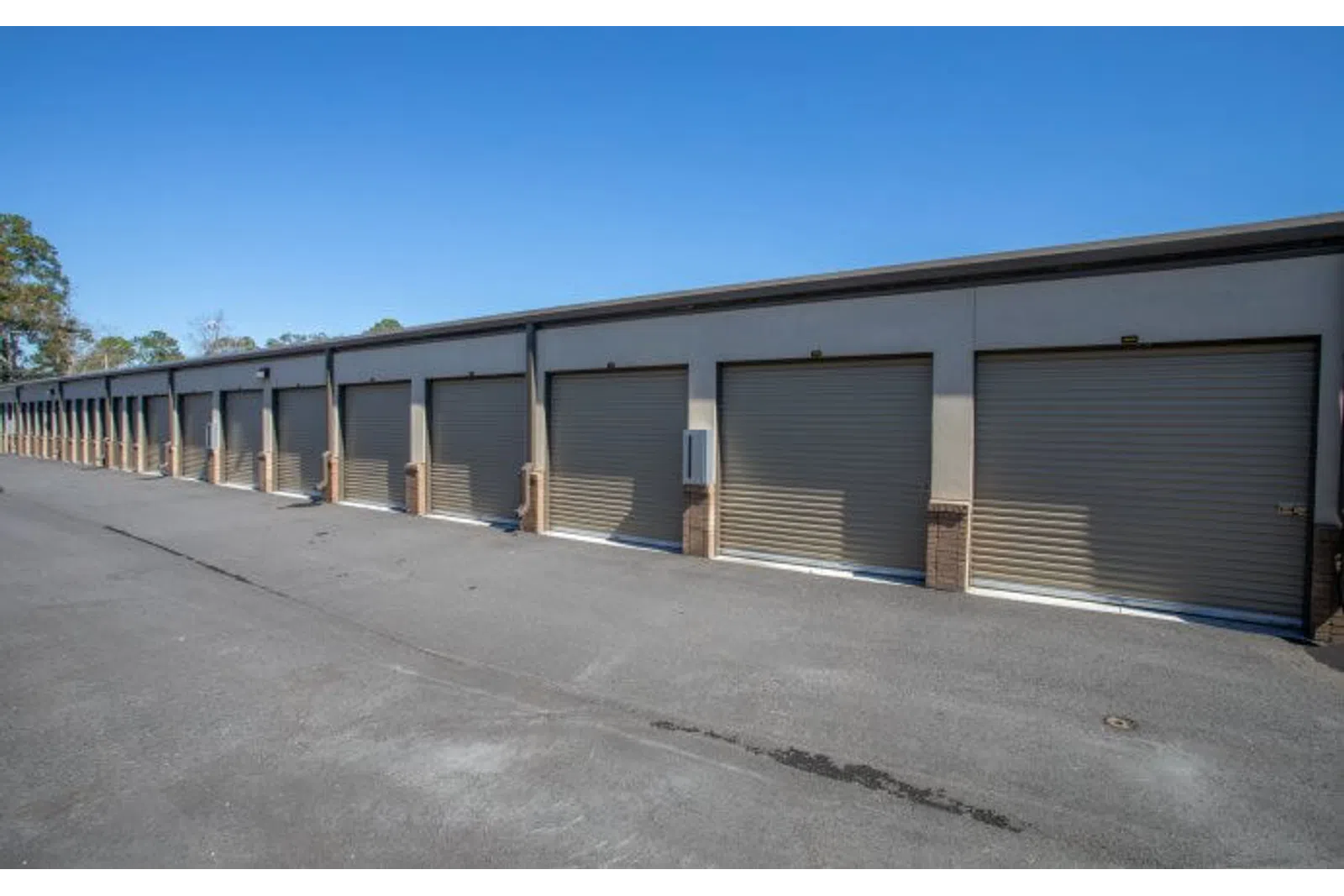 Row of closed beige storage unit doors along a paved driveway under clear blue sky.