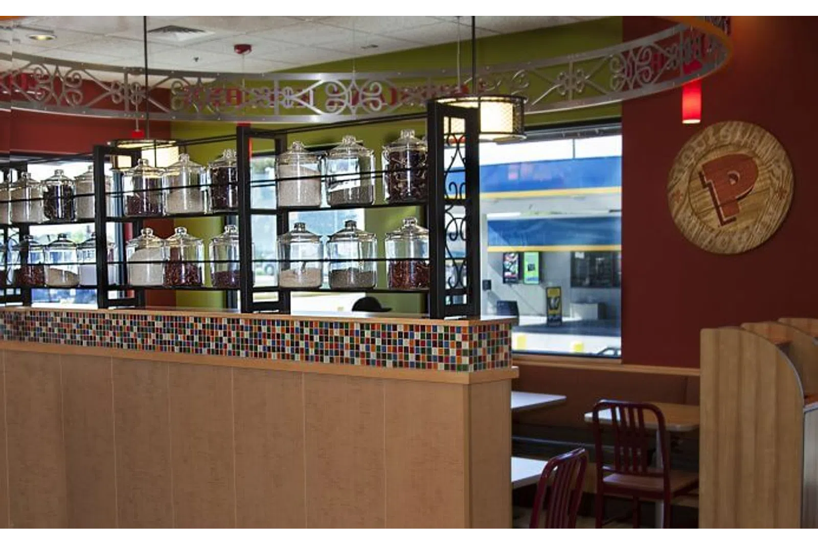 Interior of a cafe with glass jars on shelves, colorful mosaic tiles, red chairs, and wooden partitions