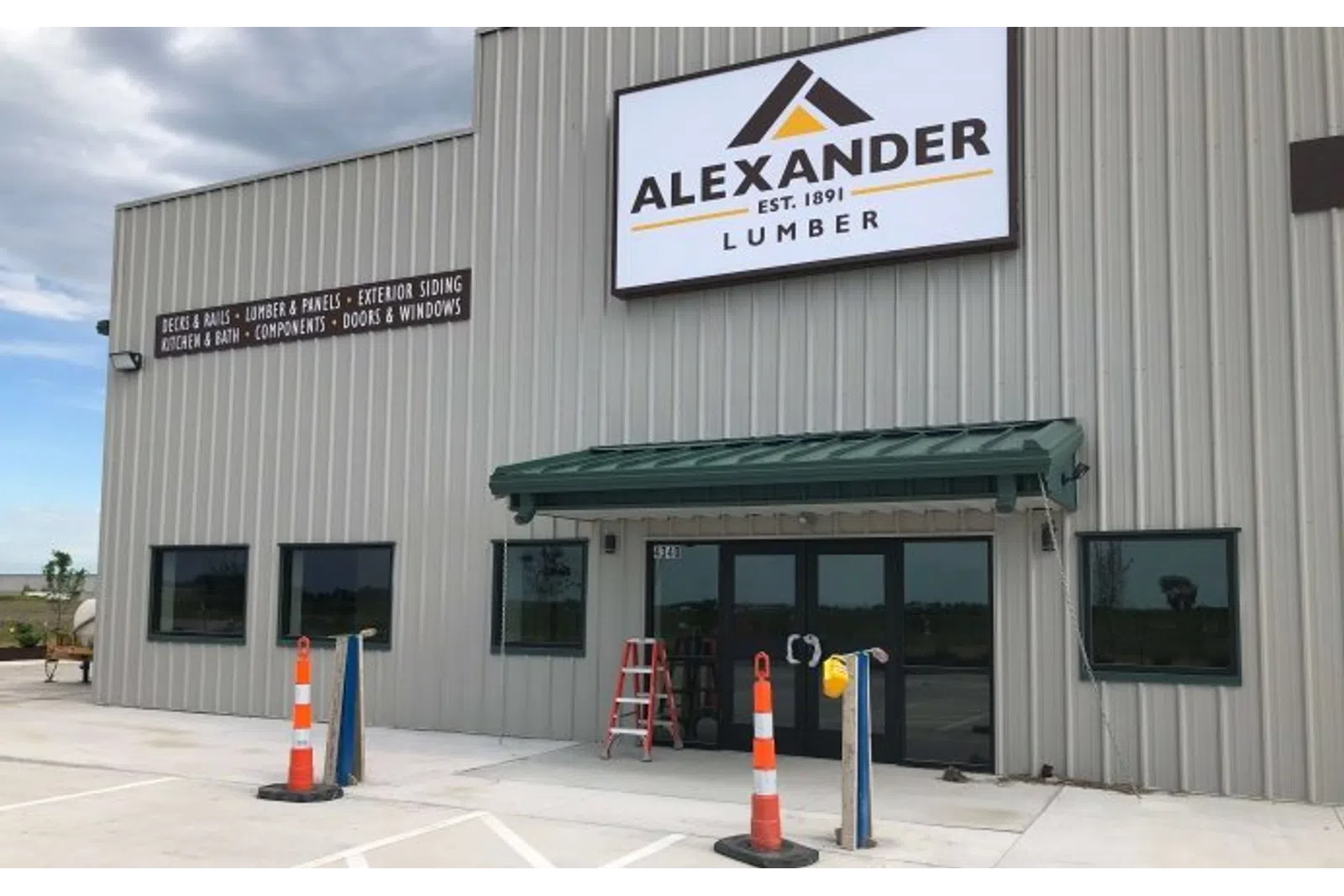 Front view of Alexander Lumber building with signage, traffic cones, and large windows on a cloudy day