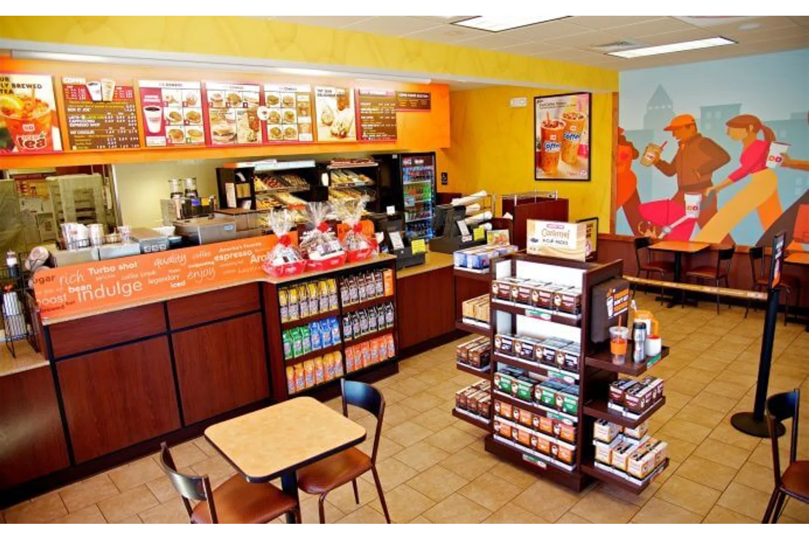 Interior view of a Dunkin' Donuts with menu boards, coffee display, and seating area including mural artwork.
