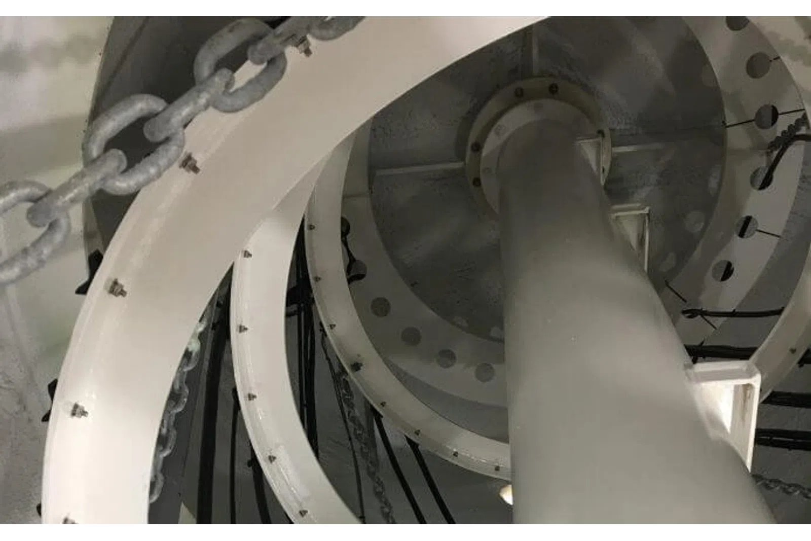 Close-up of industrial white spiral staircase with metal chains and bolts inside a structure.