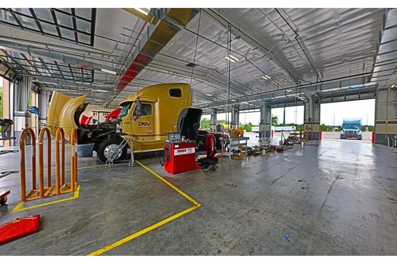 Large yellow truck undergoing maintenance inside a spacious, well-lit truck service garage with equipment and open bays.