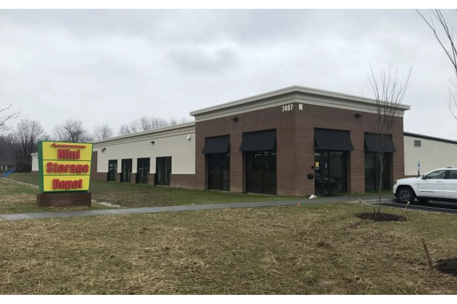 Mini Storage Depot building with black awnings and yellow-red sign on lawn under cloudy sky