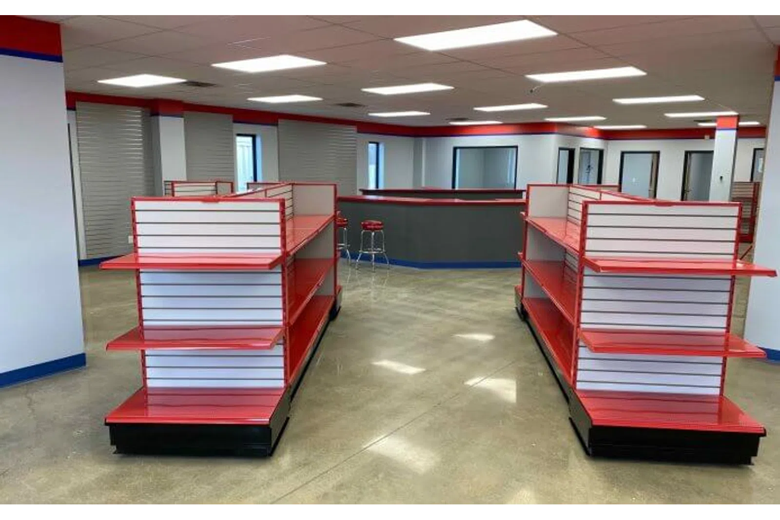 Empty red and white retail display shelves in a spacious, well-lit store interior with polished concrete floors