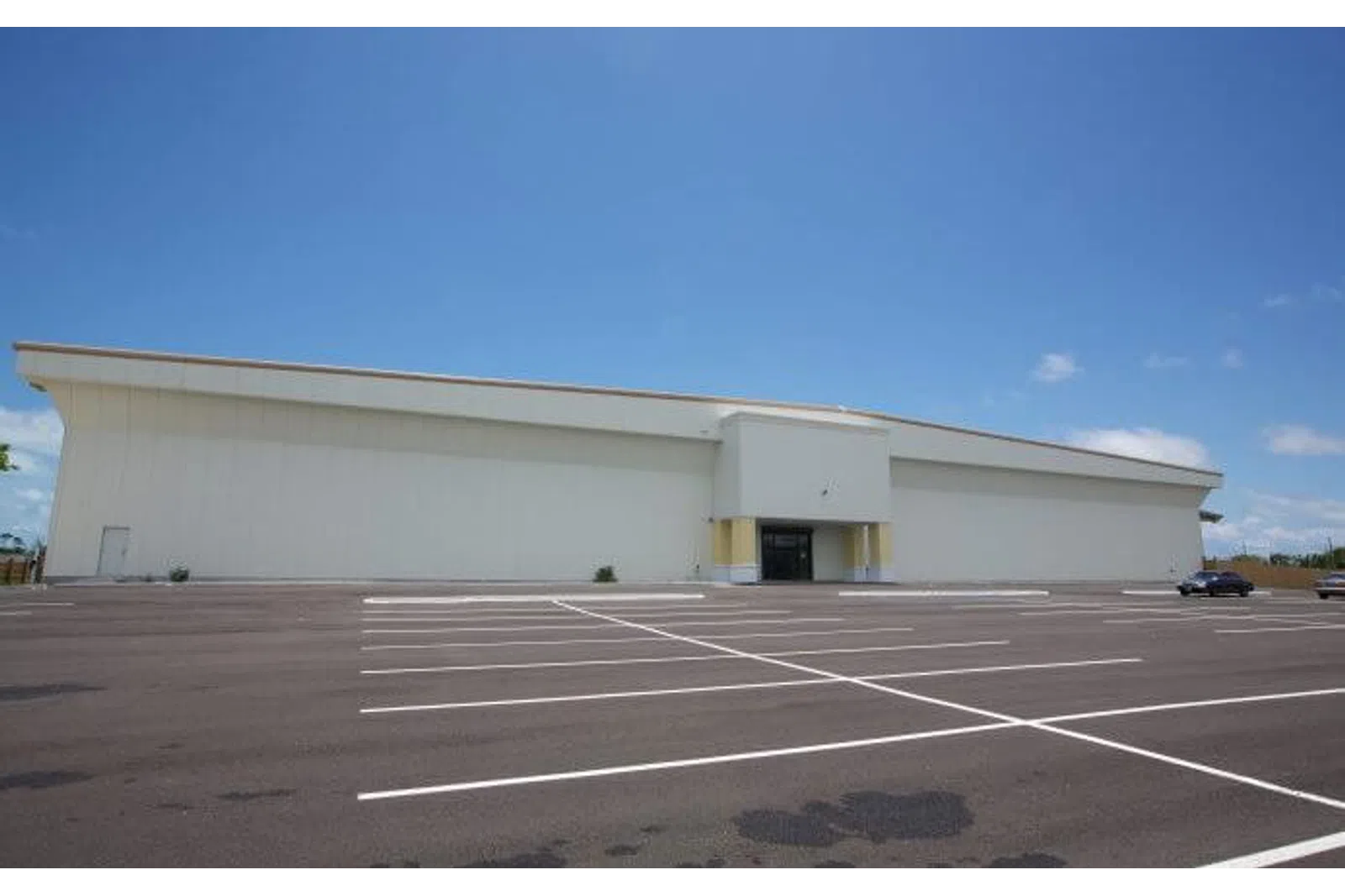Empty parking lot in front of a large white commercial building under a clear blue sky.