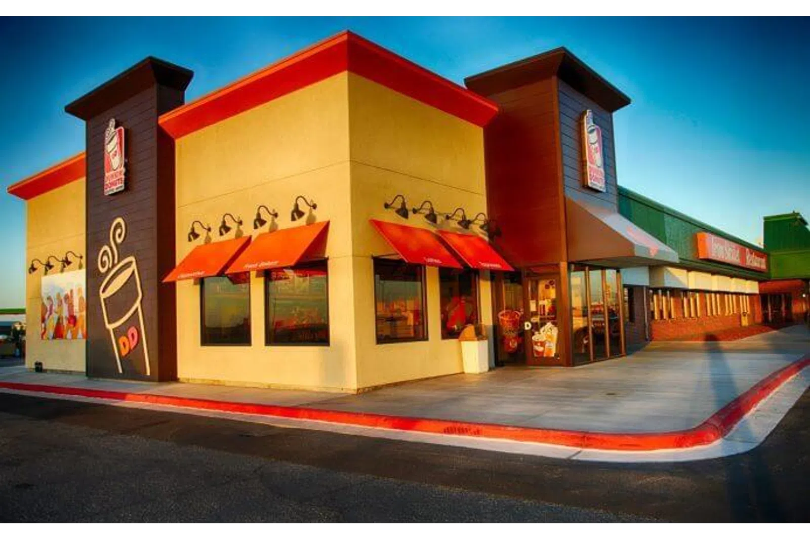 Dunkin' Donuts store exterior with red awnings and signage under clear blue sky at sunset.