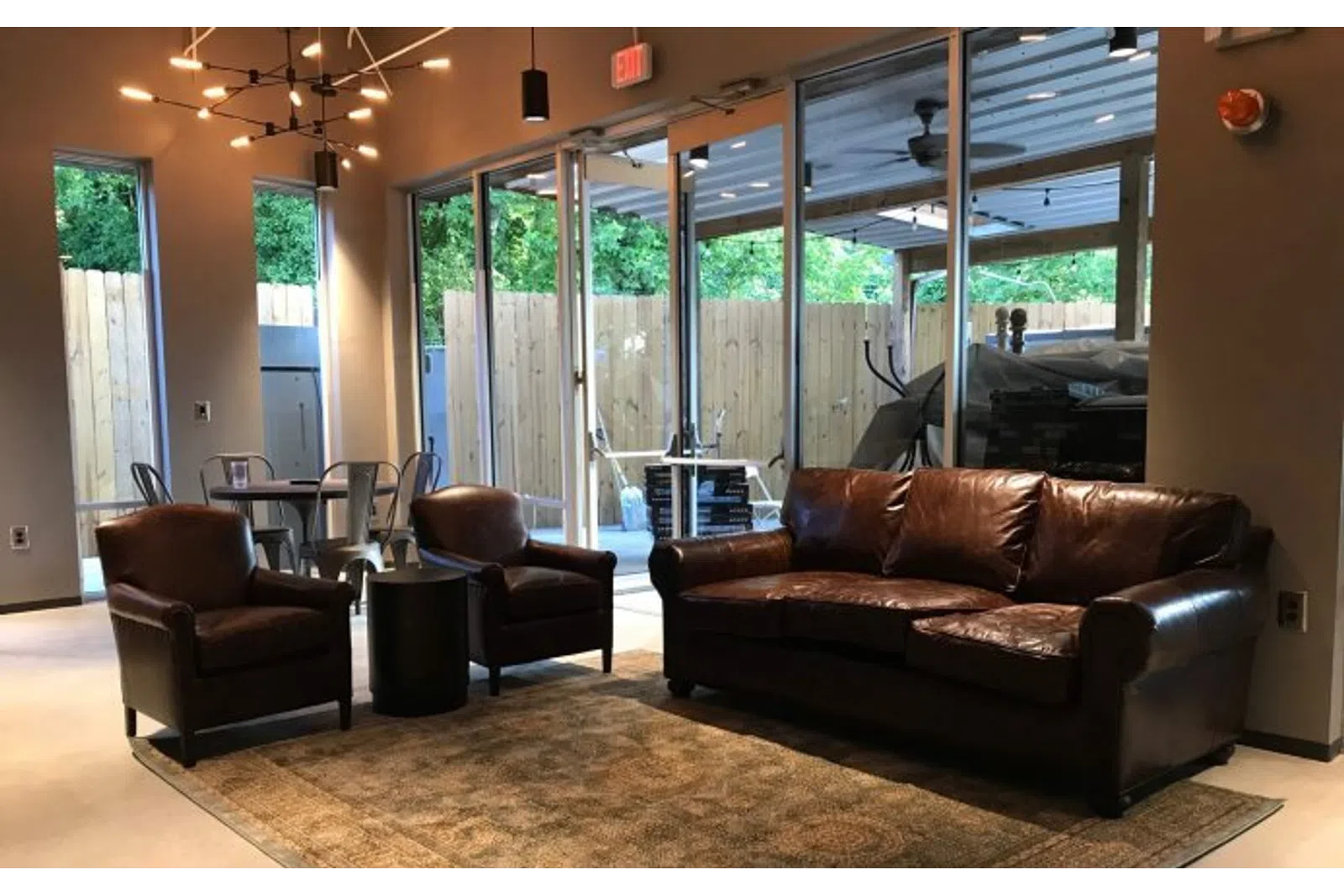 Cozy living room with brown leather sofa, two armchairs, round black table, rug, and large glass doors to outside.