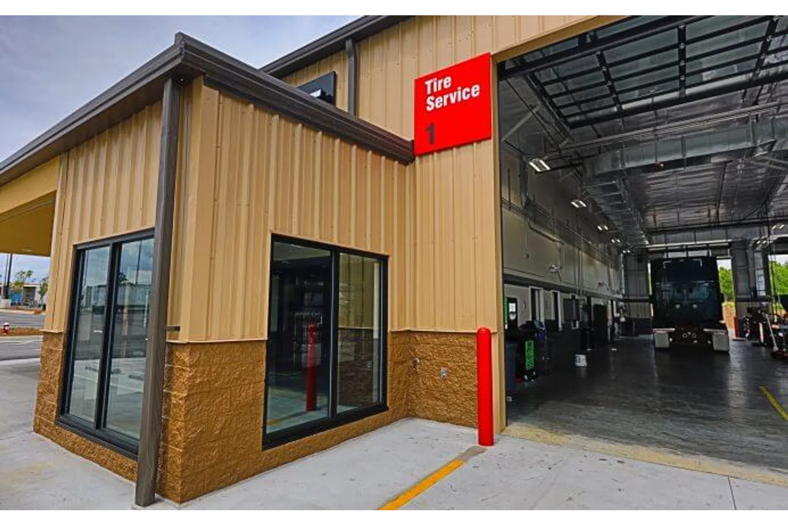 Exterior view of a commercial tire service garage with an open bay and signage under clear sky.