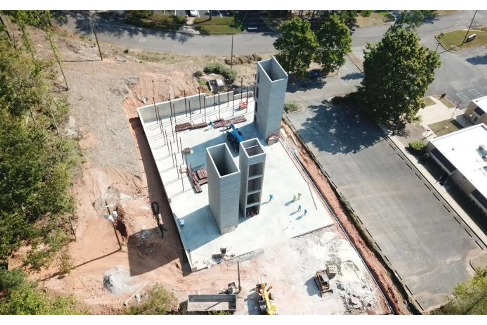 Aerial view of early-stage concrete building construction with tall vertical structures and surrounding cleared land.