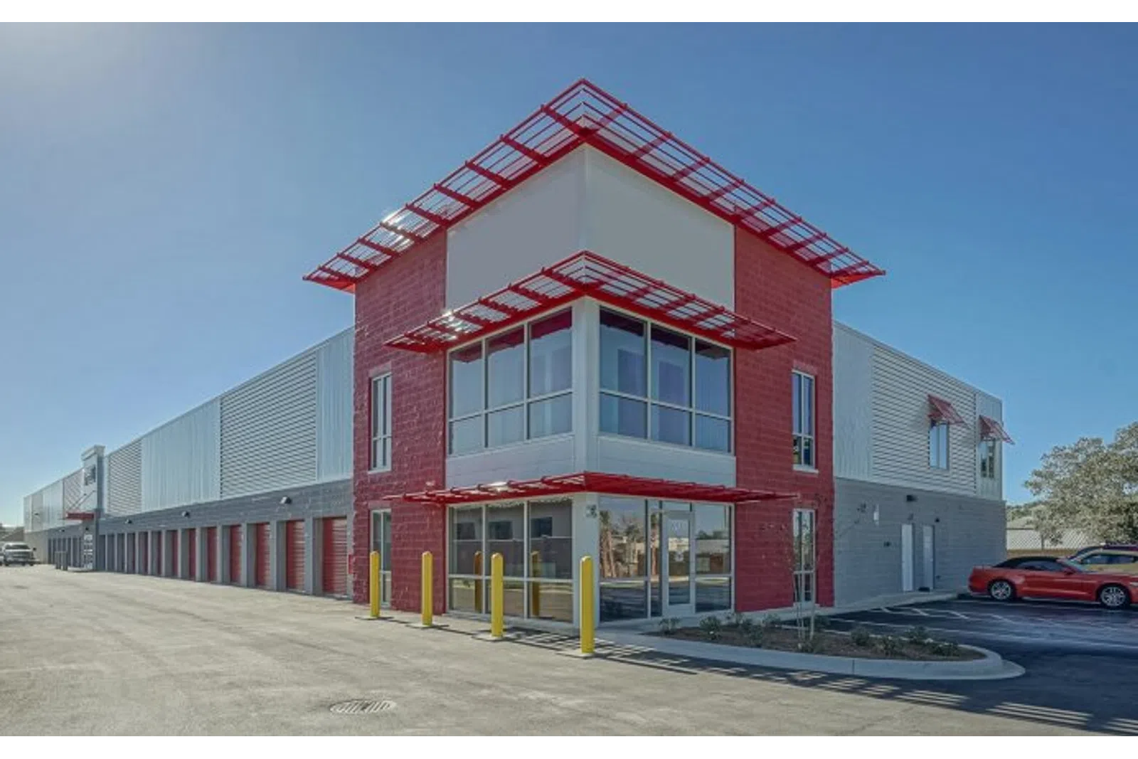 Modern commercial building with red and gray exterior, large windows, and adjacent parking under clear blue sky