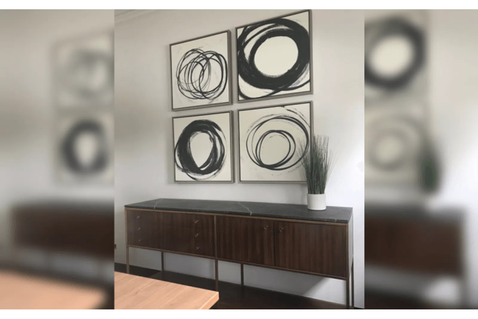 Modern interior with wooden sideboard, black marble top, potted plant, and four abstract black and white circle paintings.