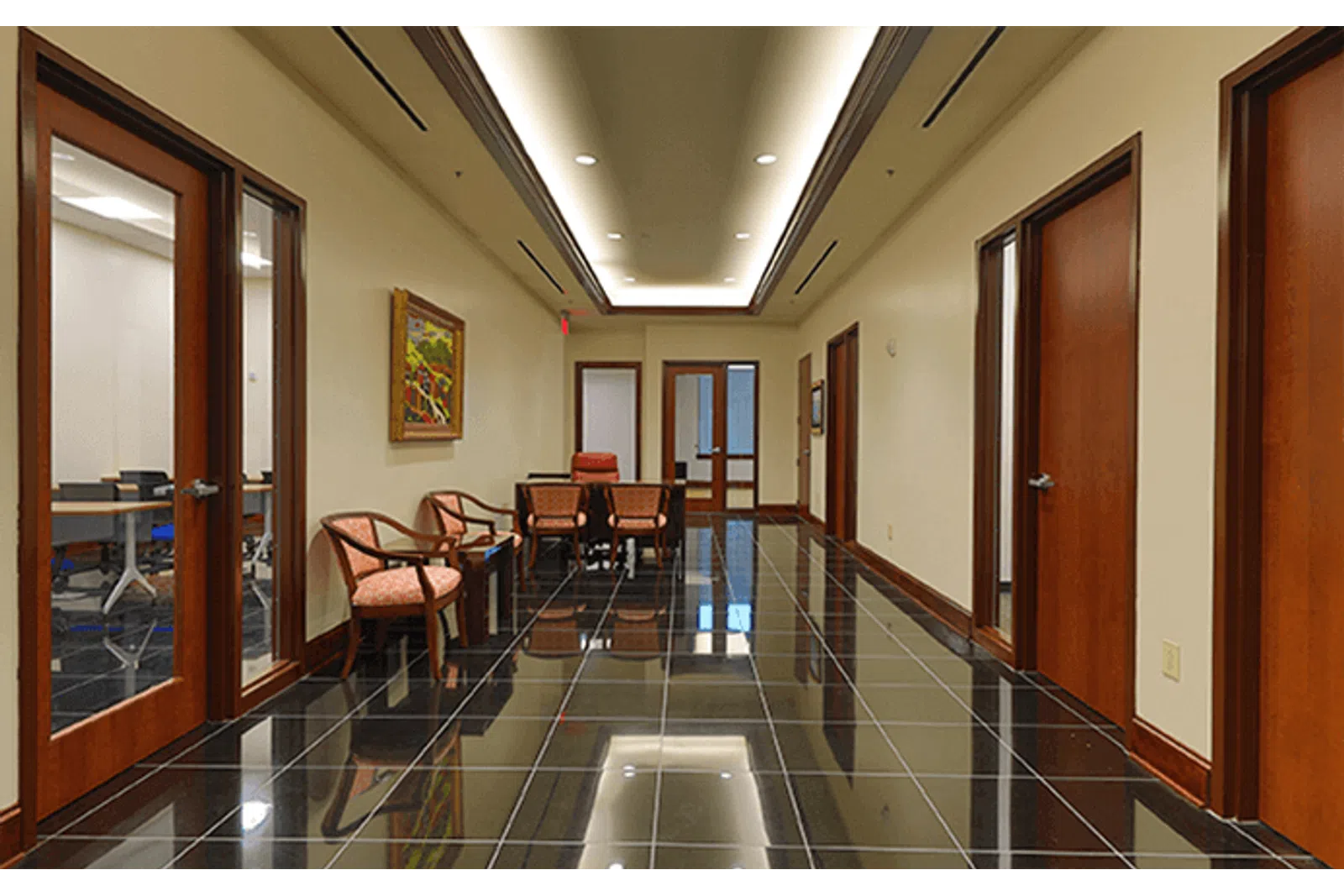 Modern hallway with glossy black tile floor, wooden doors, beige walls, chairs, and recessed ceiling lights.
