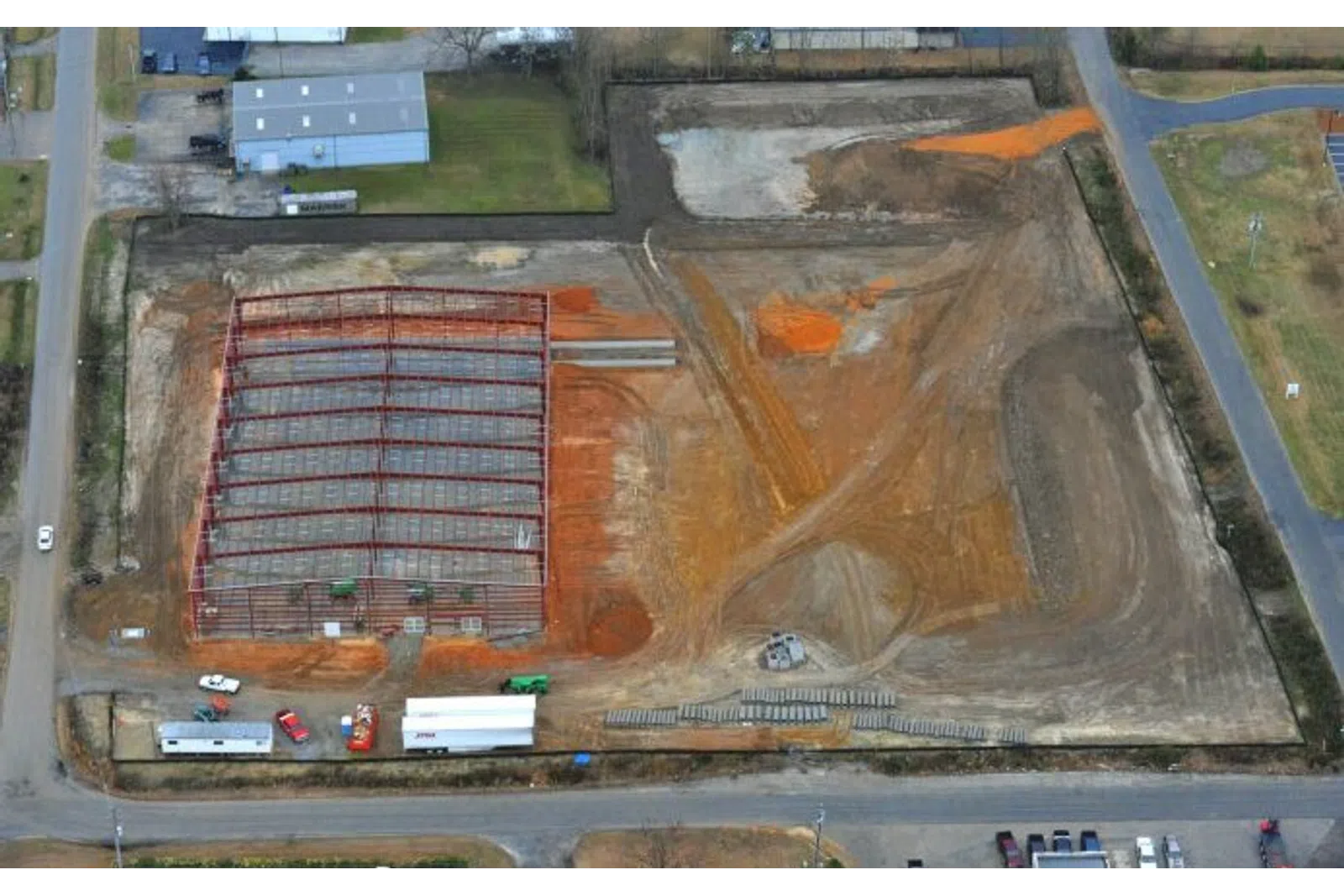 Aerial view of a construction site with steel framework erected and cleared land around it on a sunny day