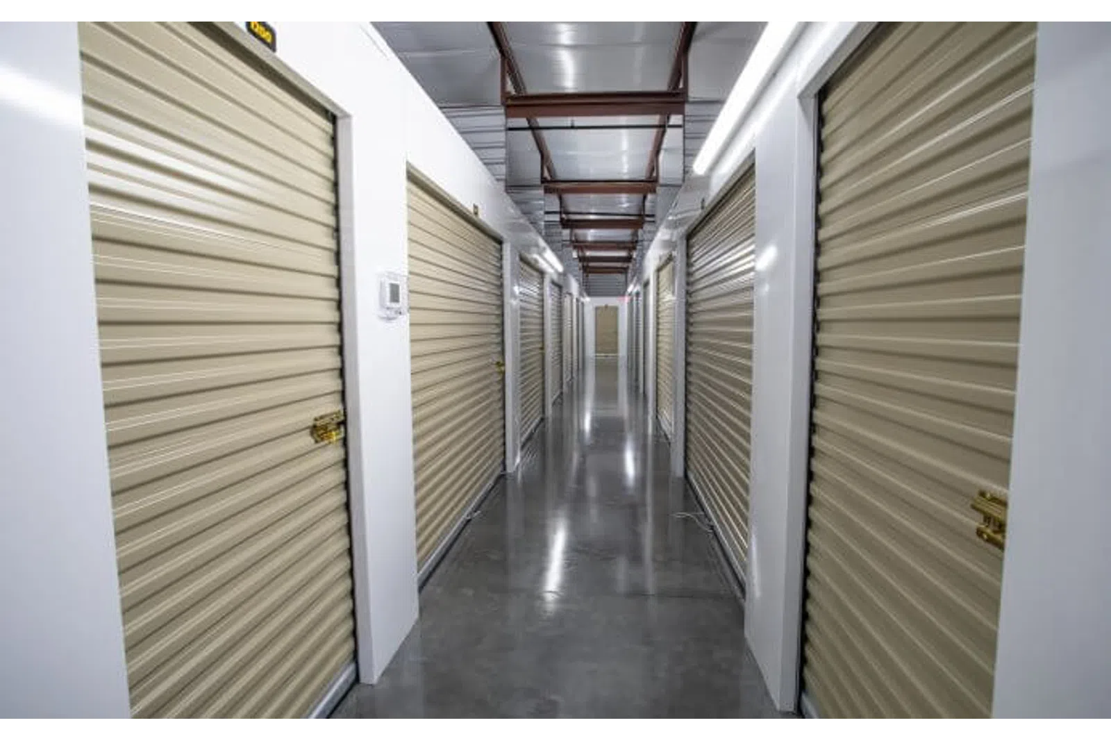 Indoor hallway of a storage facility with closed beige roll-up doors on both sides and polished concrete floor