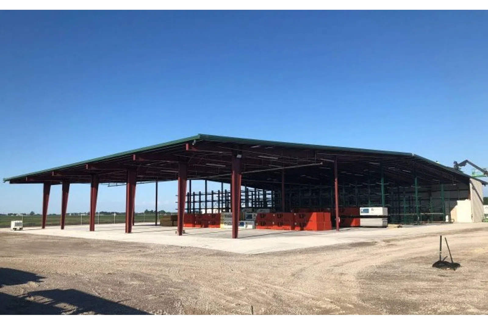 Steel-framed open warehouse under construction with a green roof on a clear sunny day in a rural area.