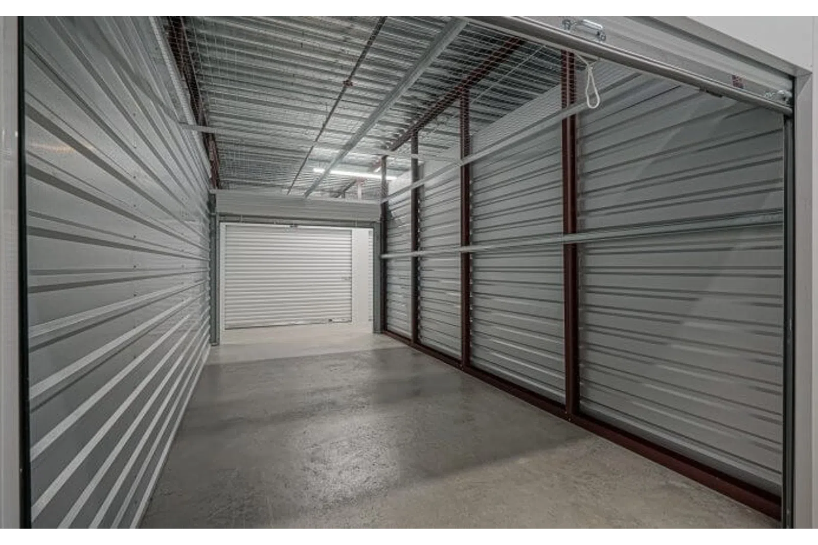 Empty indoor storage unit with metal walls and concrete floor under overhead lighting.