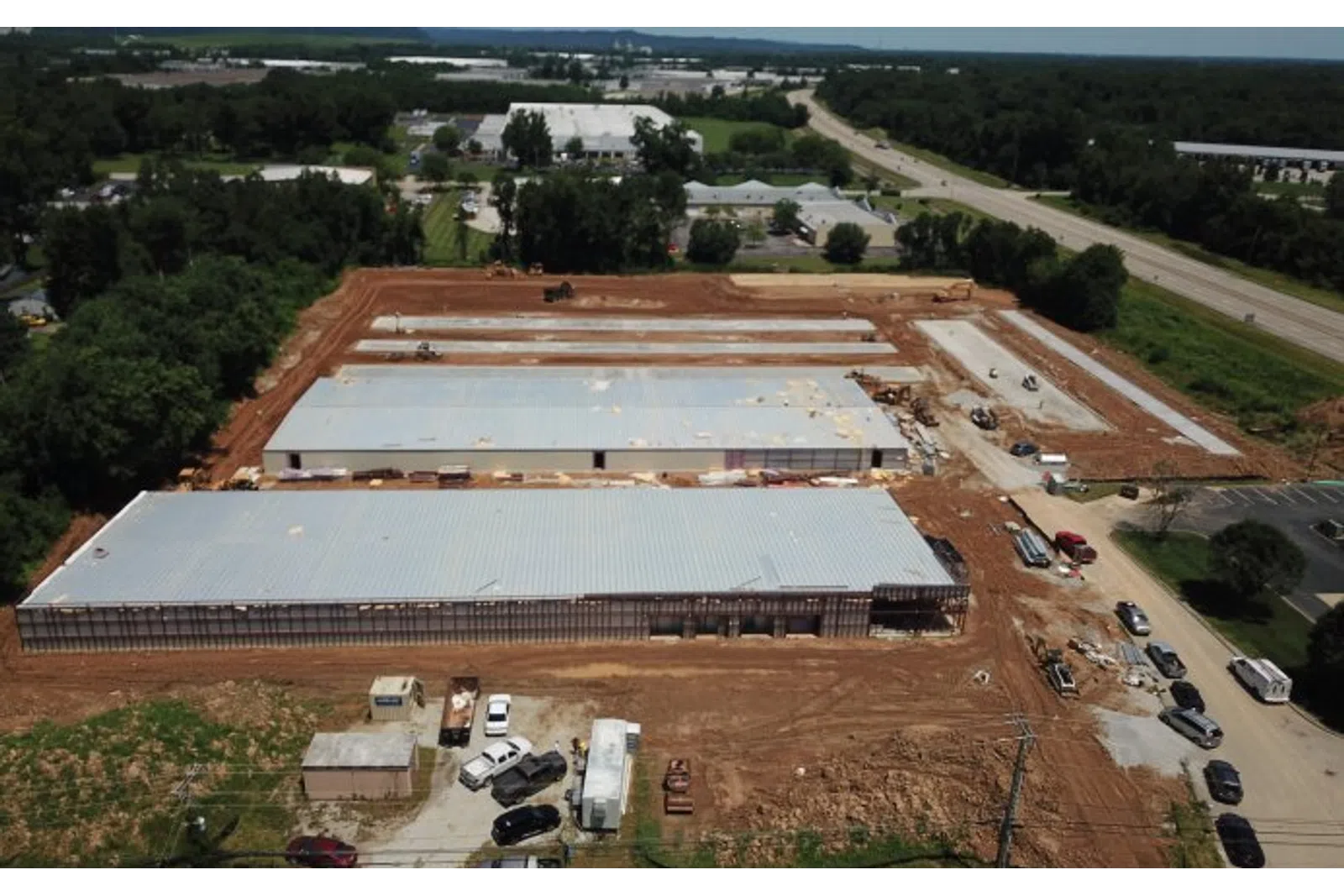 Aerial view of a large industrial warehouse construction site with metal roofs and surrounding cleared land.