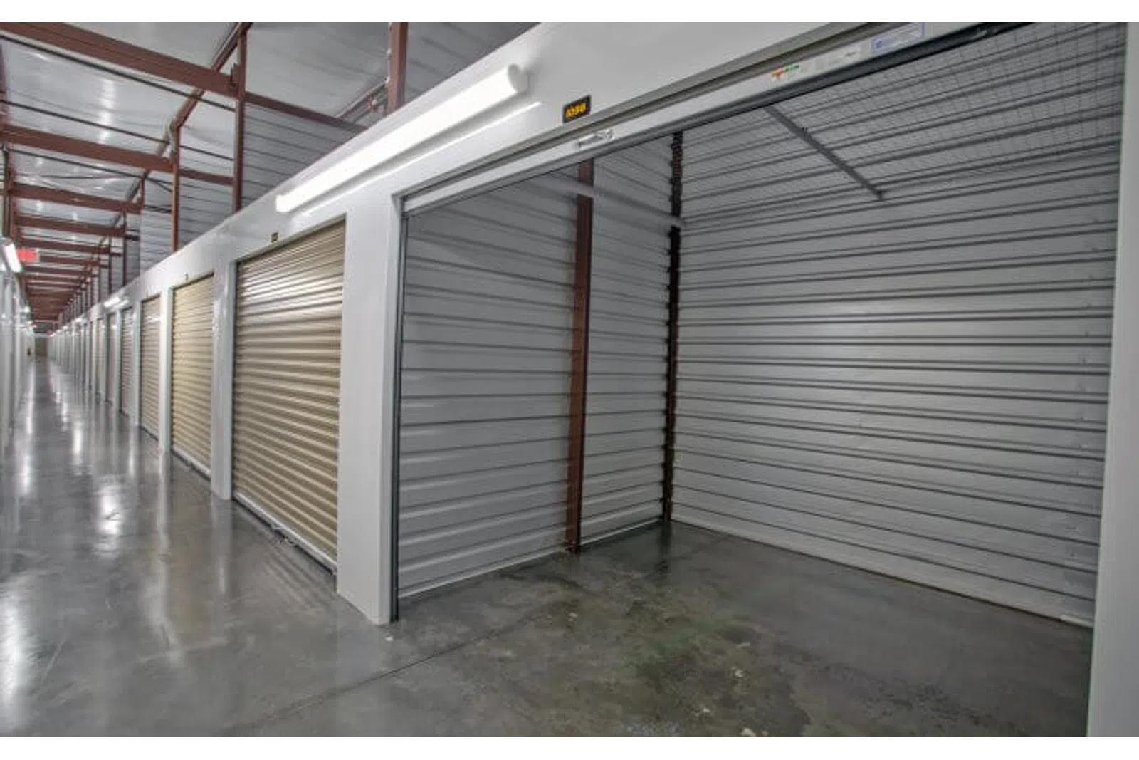 Interior view of a self-storage facility with open and closed metal roll-up doors and polished concrete floors.