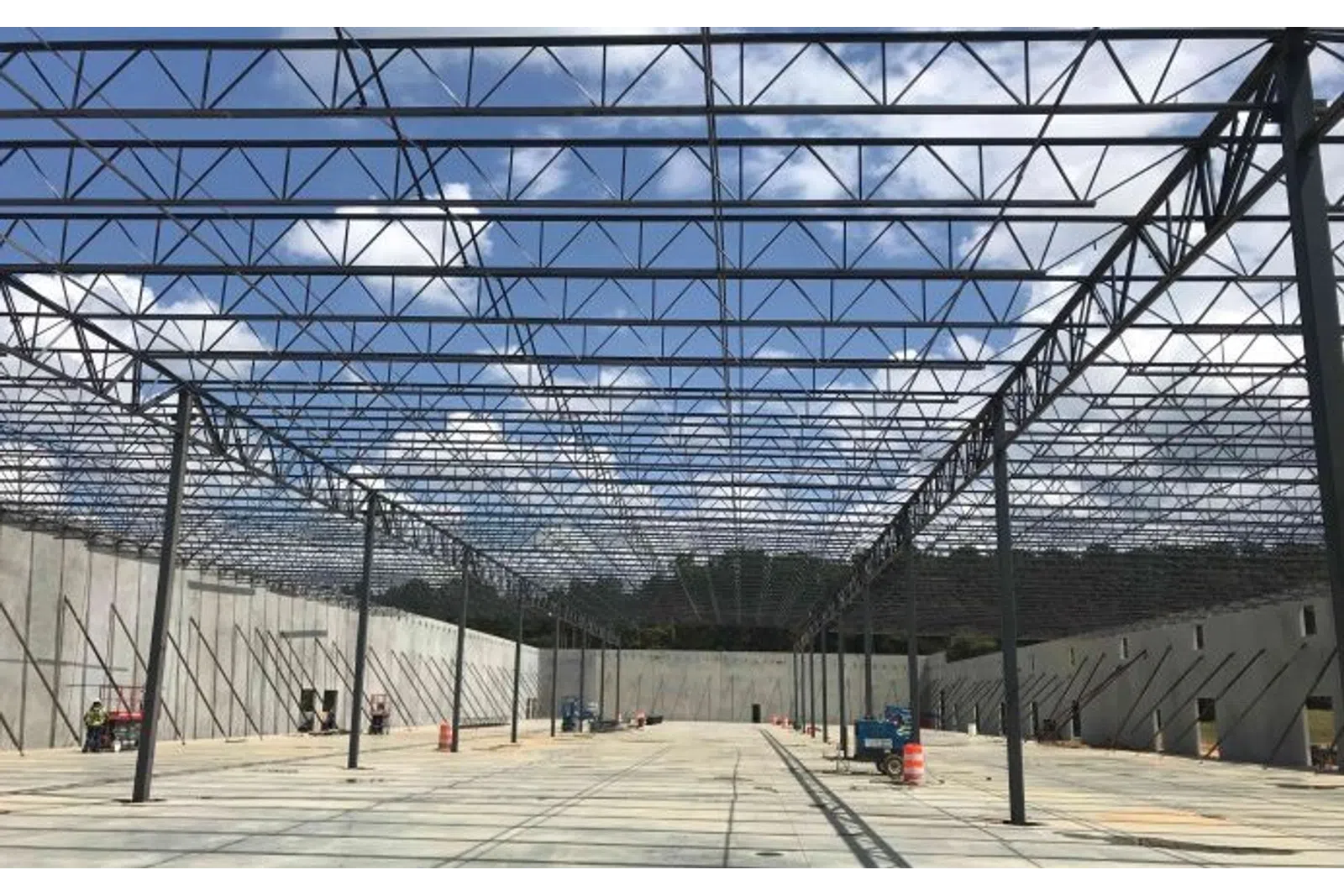 Steel framework and concrete walls of a large industrial building under construction with clear blue sky.