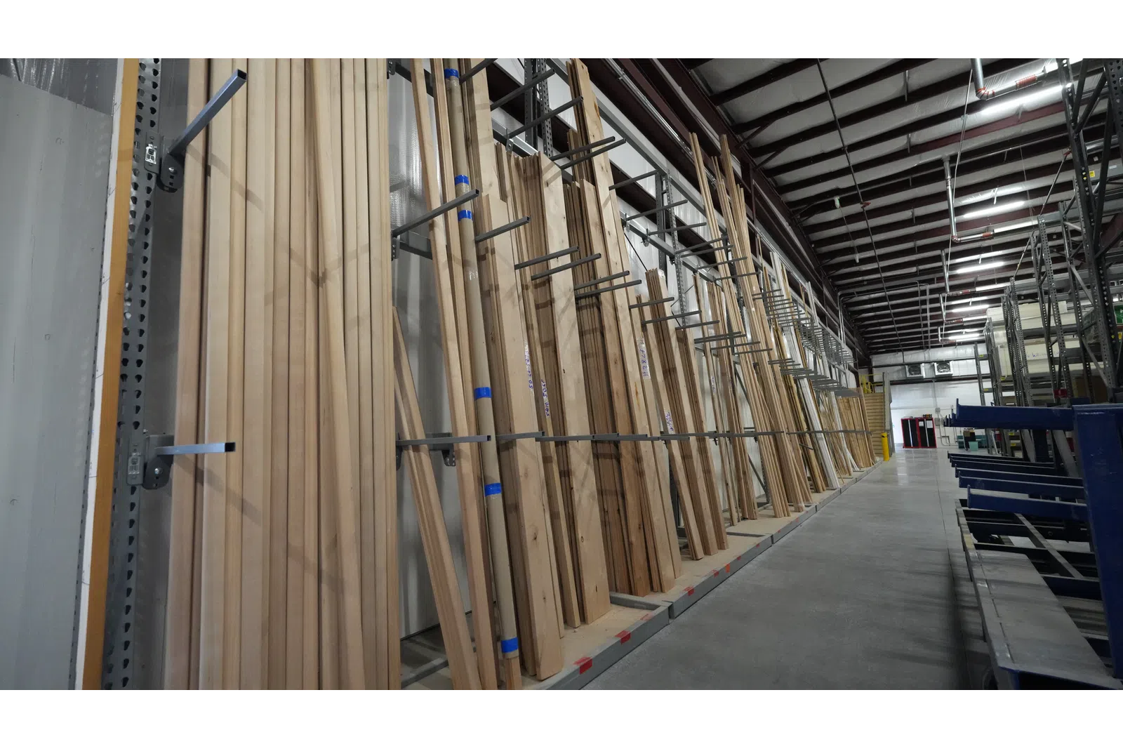 Rows of wooden planks neatly organized on metal racks inside a spacious warehouse with concrete floors.