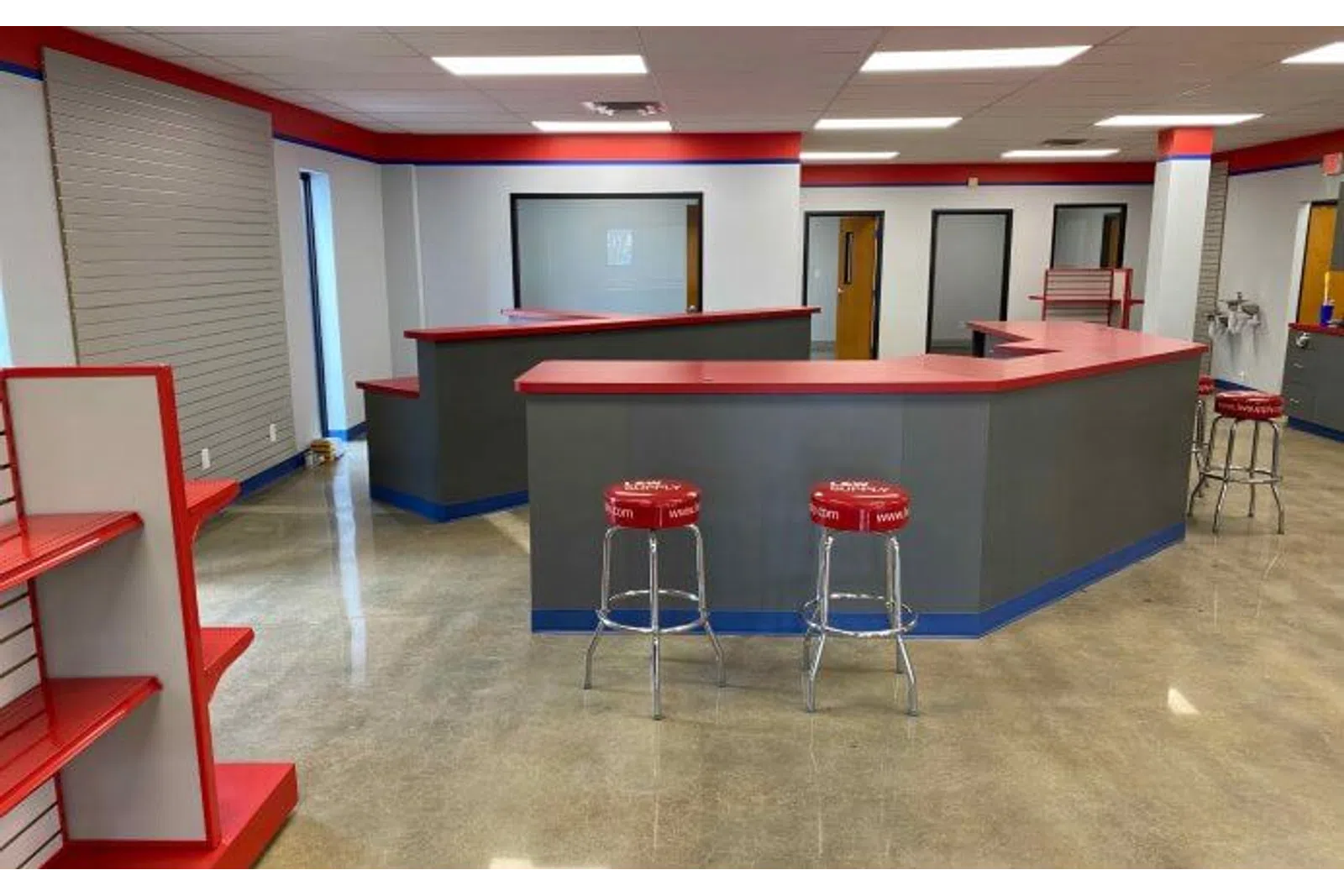 Modern commercial space with red and gray counters, stools, shelving, and polished concrete floor.