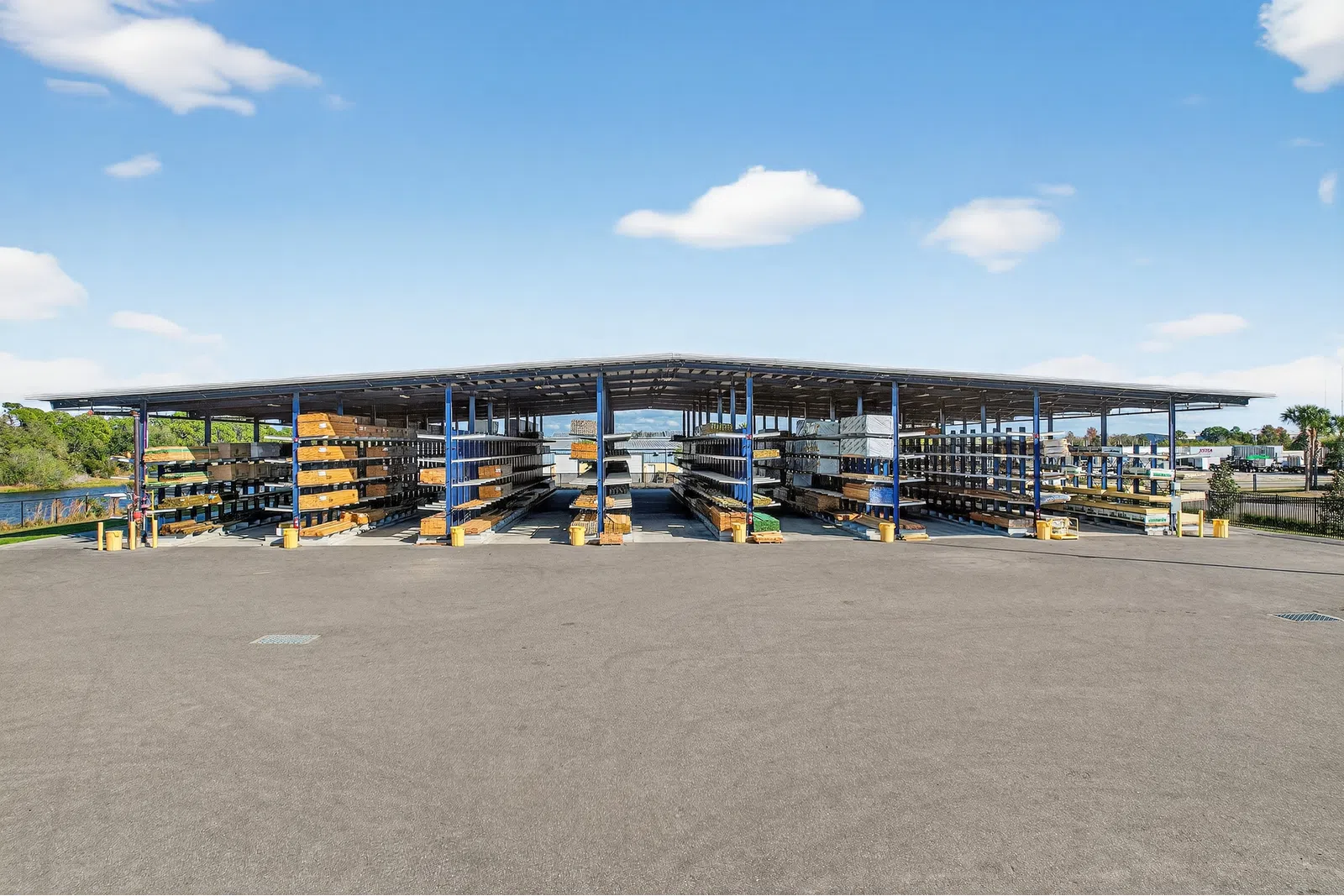 Outdoor storage rack with various lumber and wood planks under a canopy on a clear sunny day.