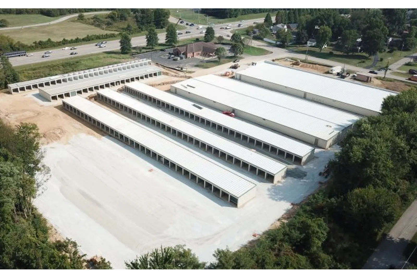 Aerial view of a large storage facility with multiple long white-roofed buildings surrounded by trees and roads.