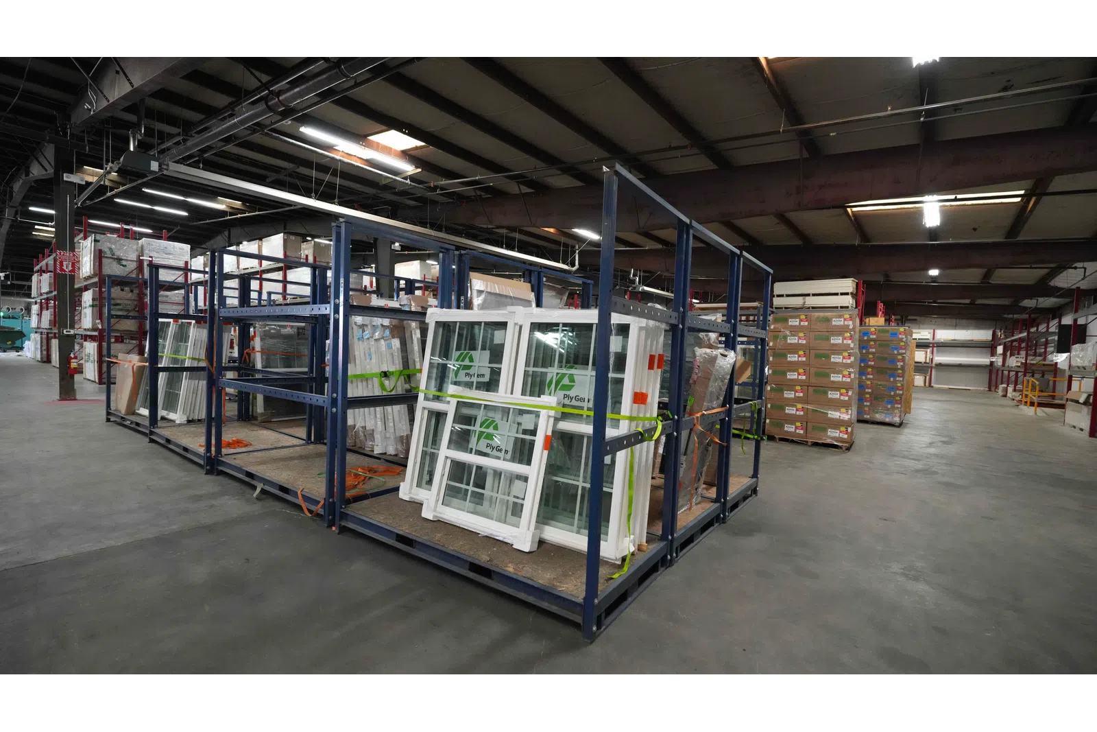 Large warehouse shelving holds packaged windows and building materials under high ceiling lights.