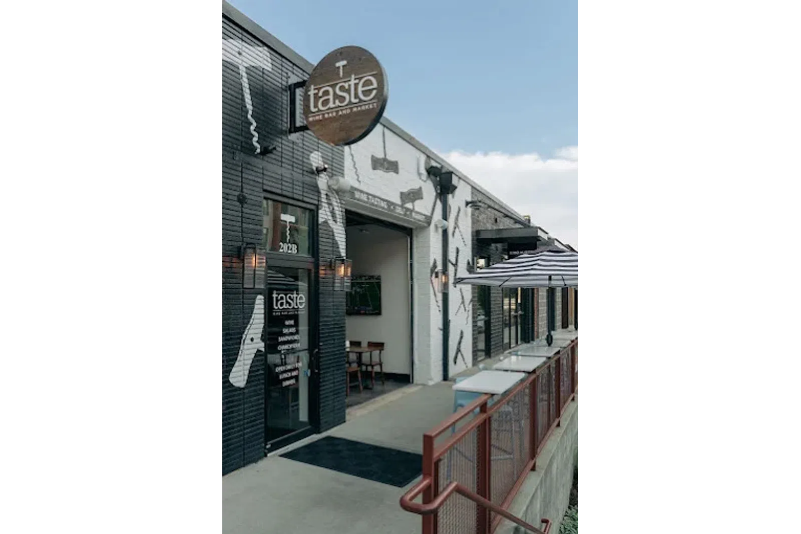 Exterior view of Taste Wine Bar and Market with black and white walls and outdoor seating under umbrella.