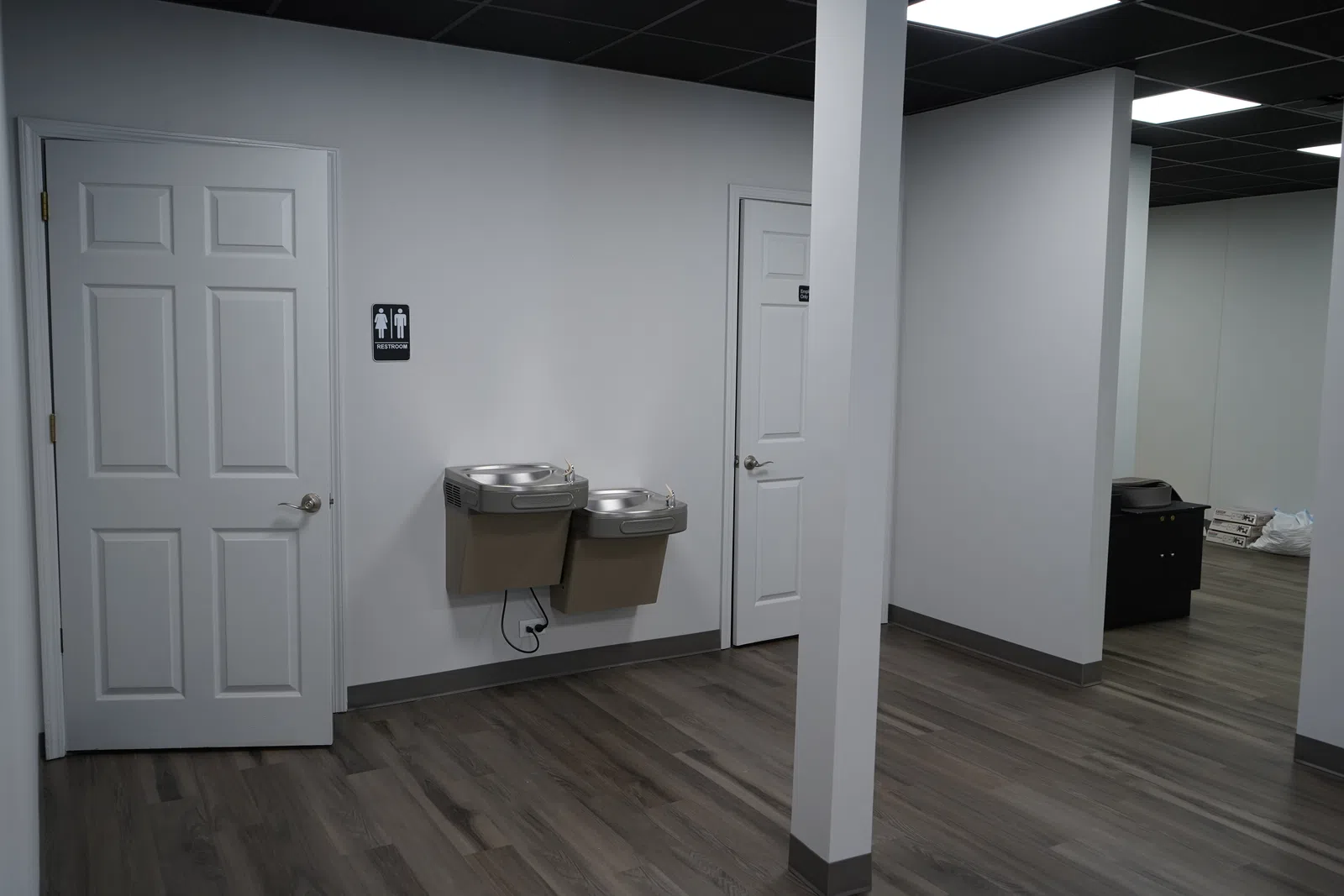 Interior of a modern indoor space with two white doors, dual water fountains, and wood-look flooring.