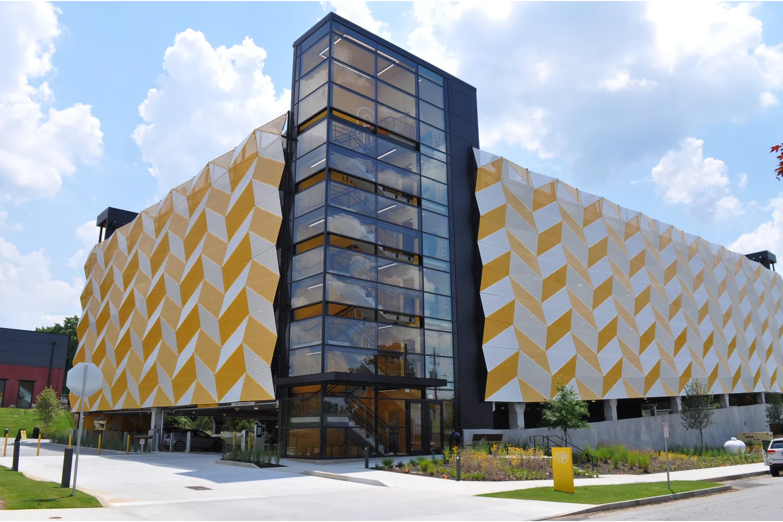 Modern parking garage with geometric yellow and white exterior panels and glass elevator shaft under a blue sky.