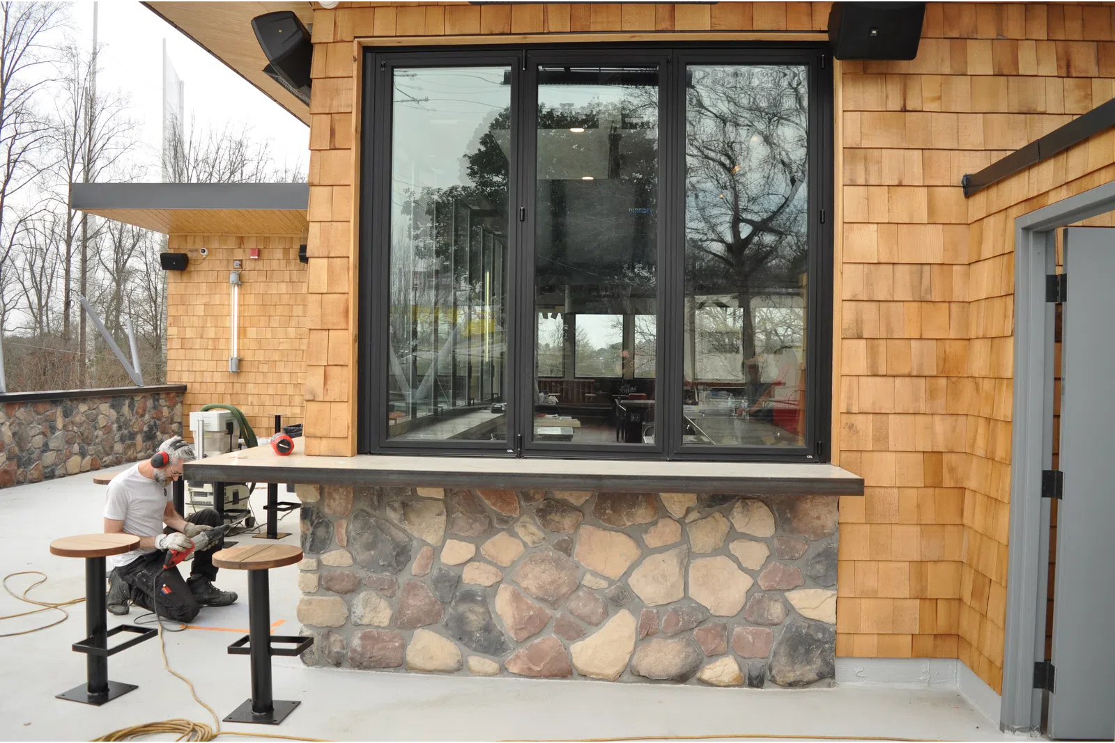 Man working on outdoor seating area with stone and wood siding during construction or renovation.