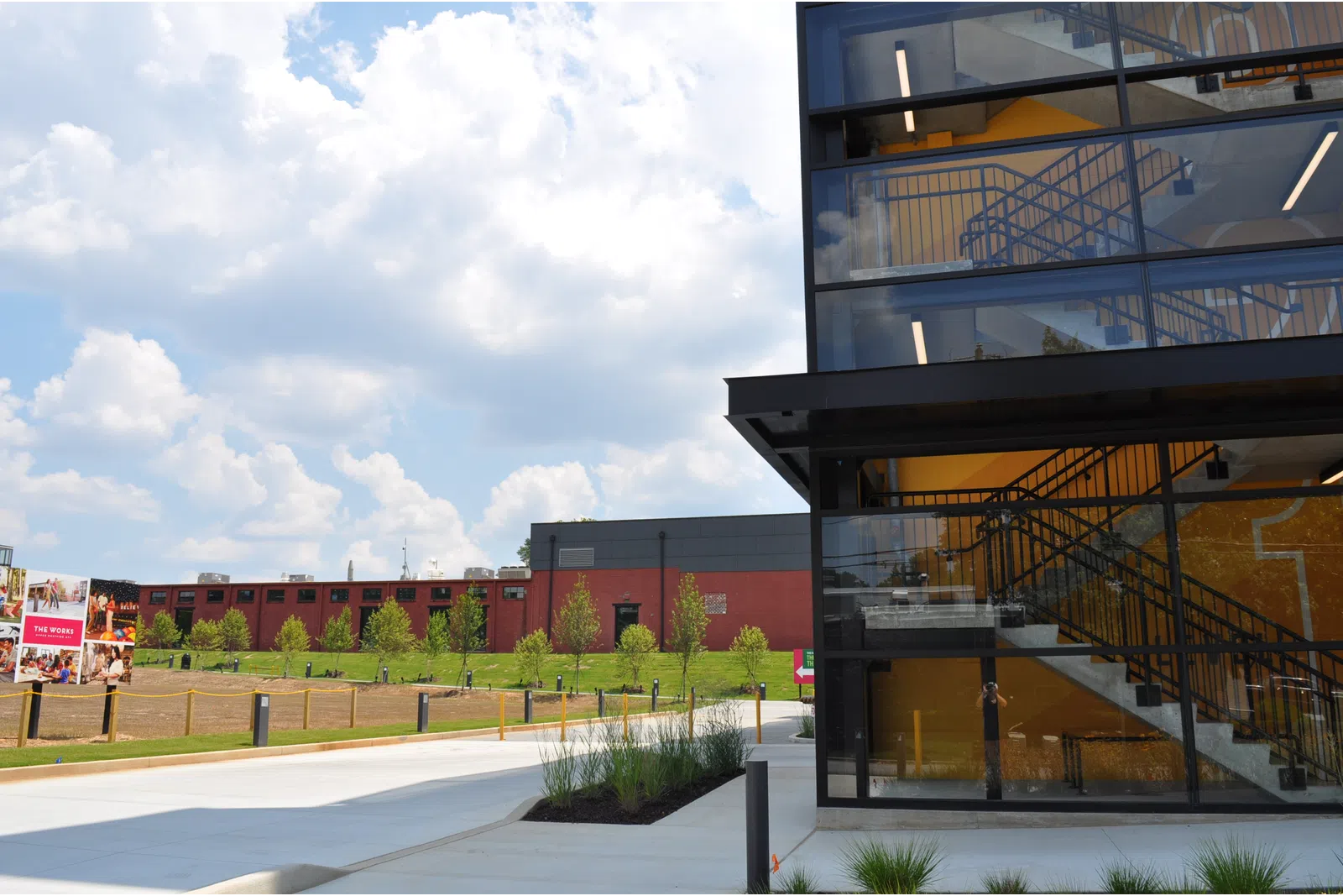 Modern building with glass windows and visible staircase next to a green lawn and partly cloudy sky.