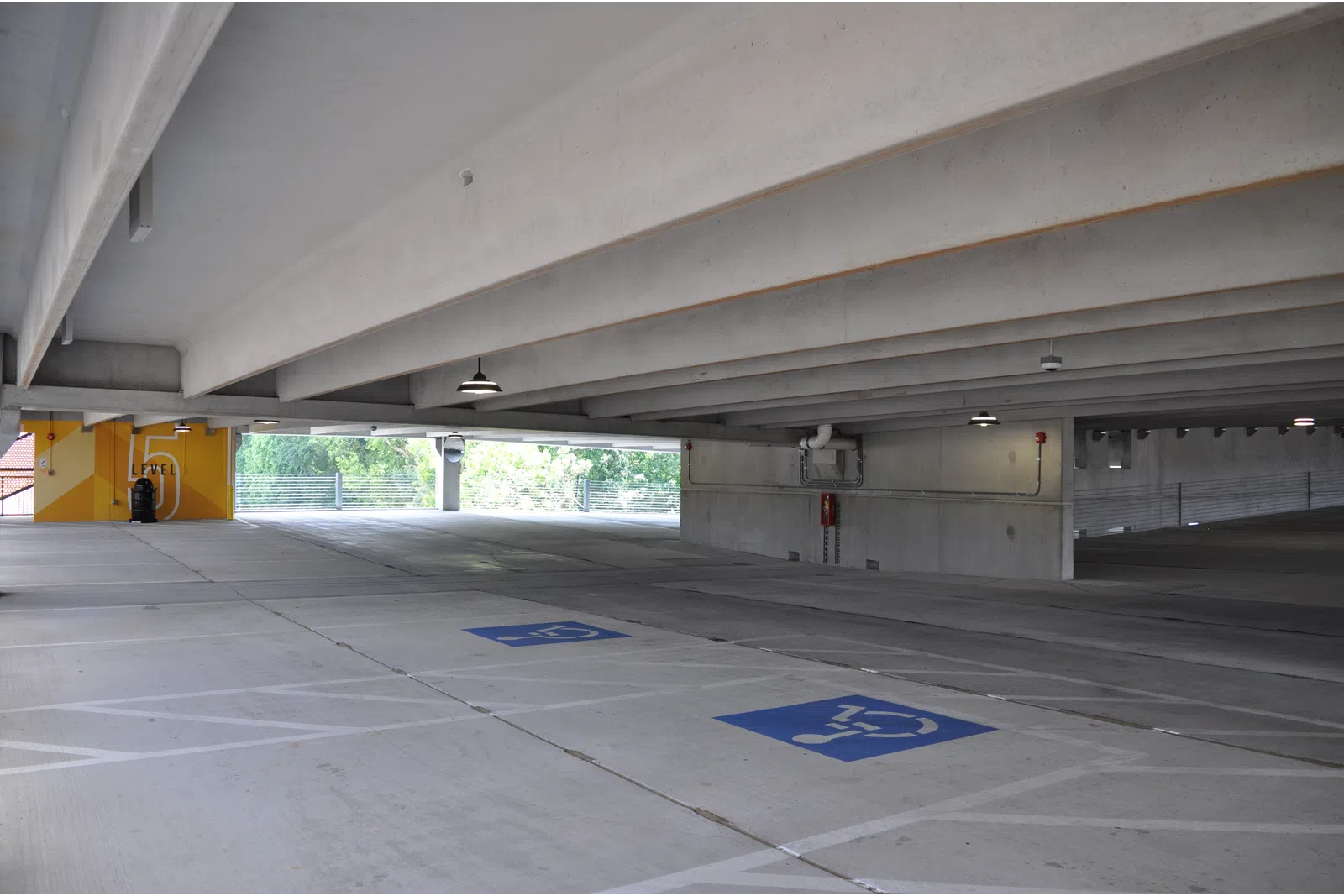 Empty concrete parking garage level with visible handicapped parking spaces and structural beams overhead.
