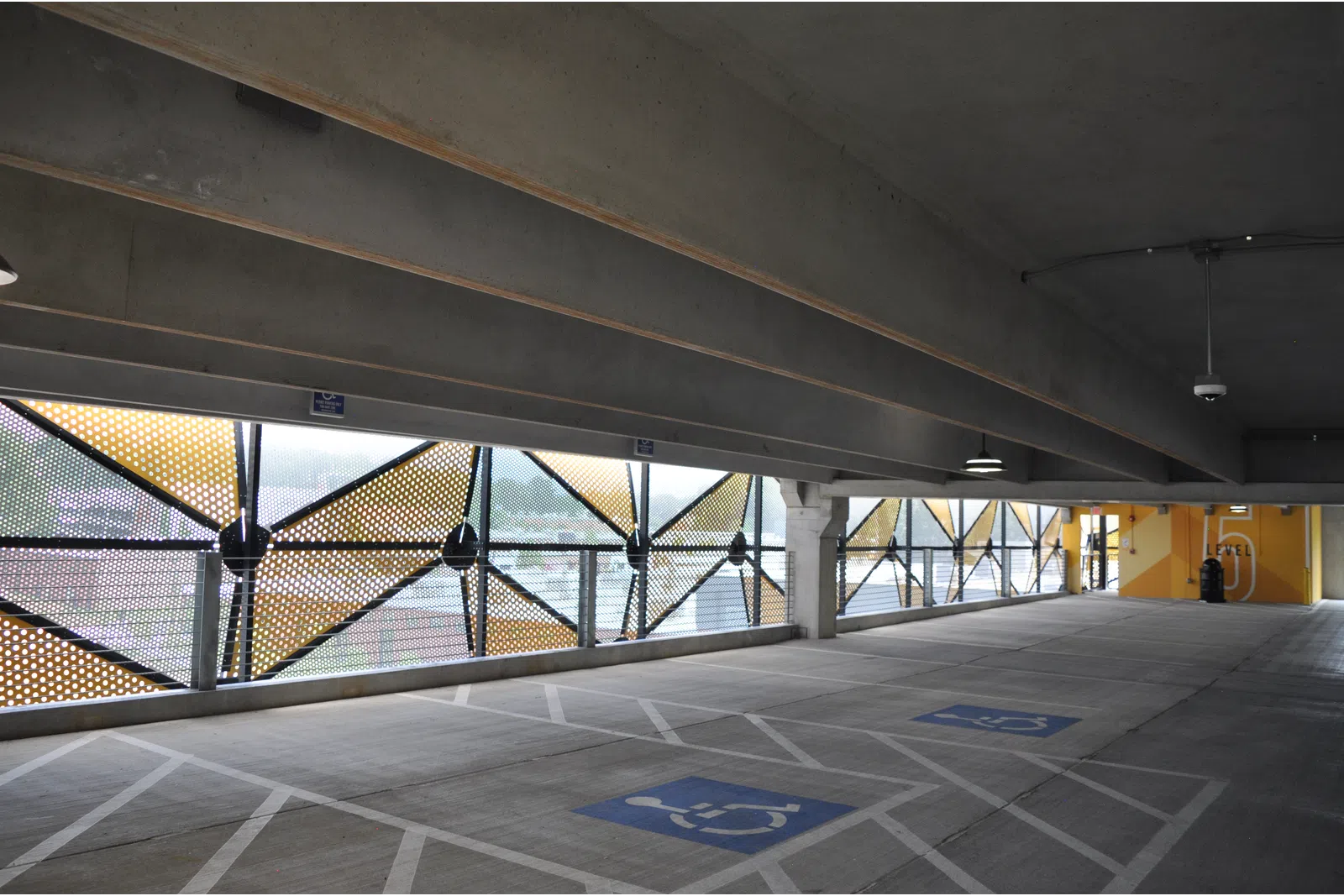 Empty indoor parking garage with handicapped spaces and perforated metal panels allowing natural light.
