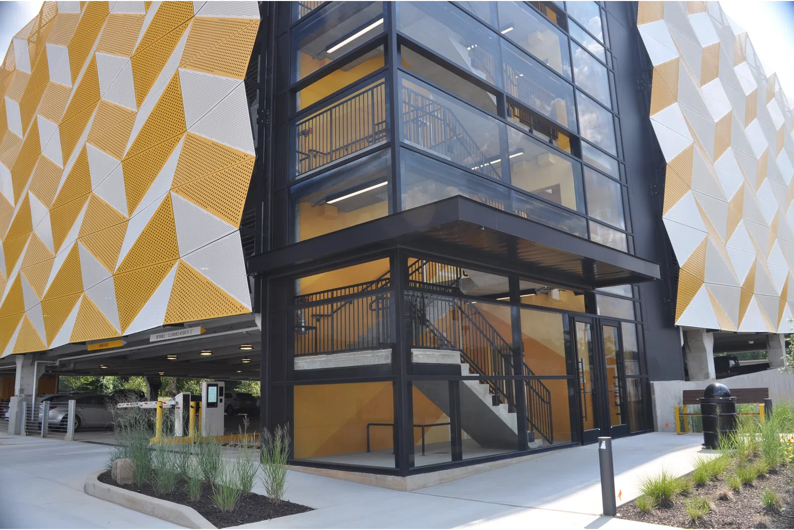 Modern parking garage exterior with geometric yellow and white panels and glass-enclosed stairwell.